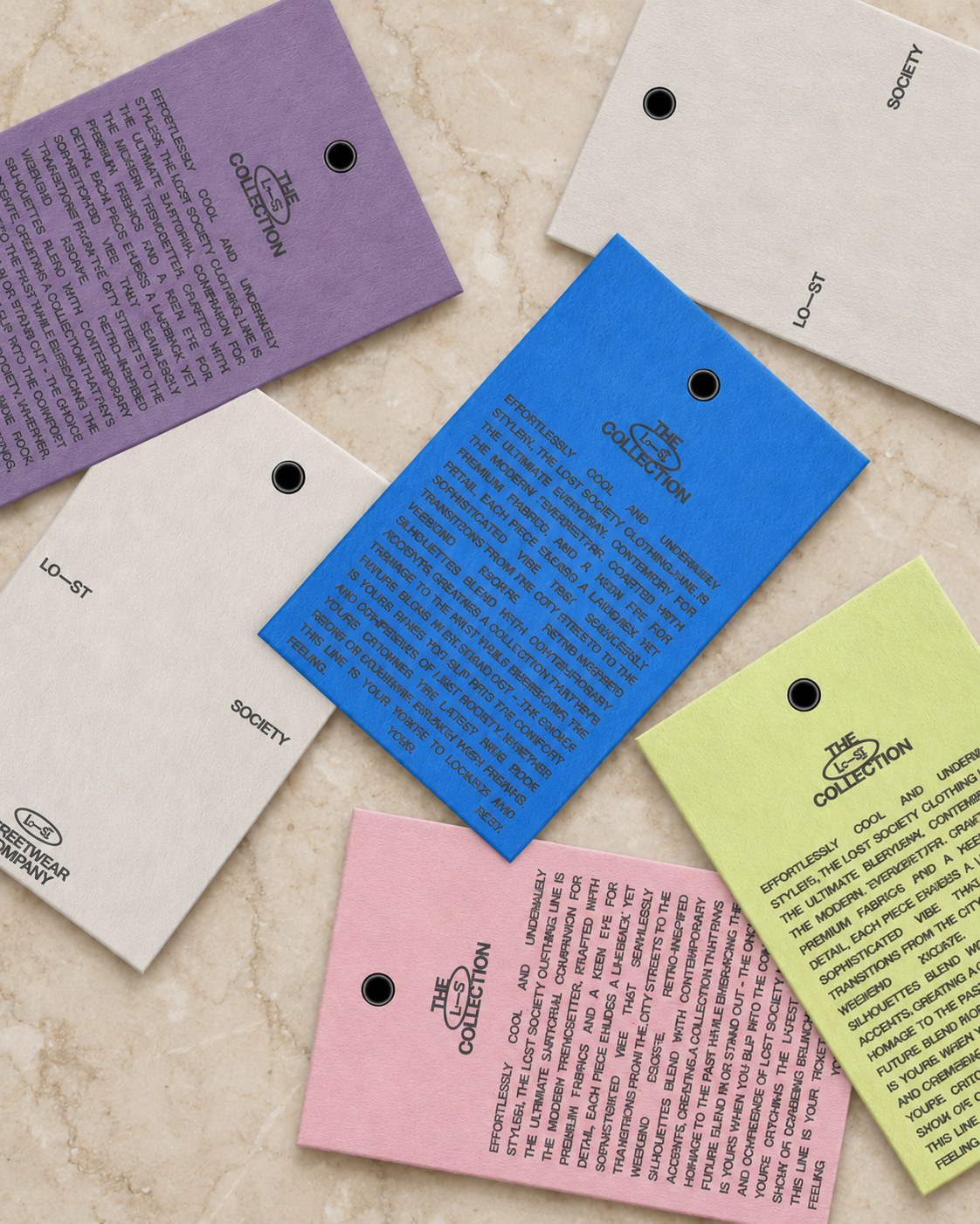 Various colored tags from 'The Effortlessly Cool Collection,' with descriptive text about fashion and society, each tagged with black eyelet holes, arranged on a marble surface.