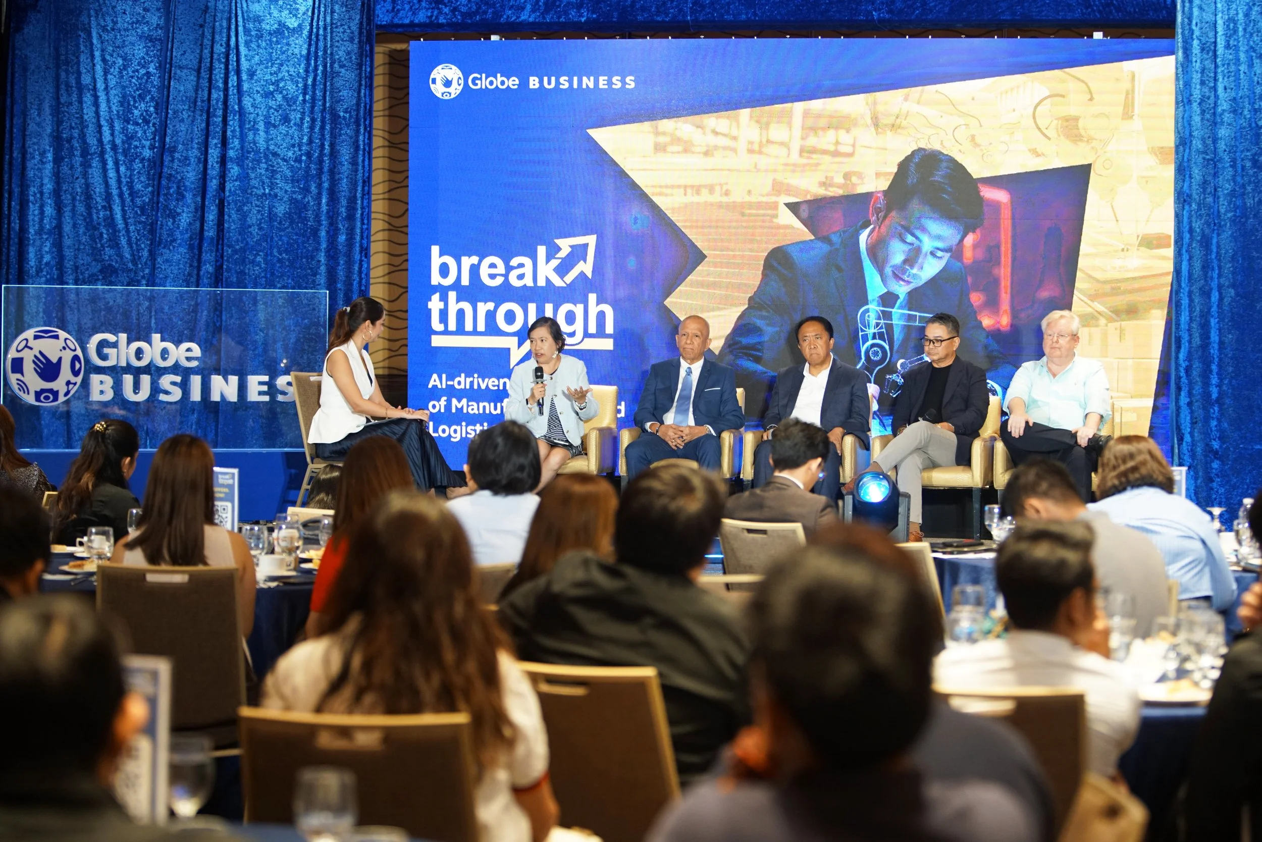 Panel discussion at a conference with a large blue screen displaying Globe Business and the words "break through" behind the speakers.