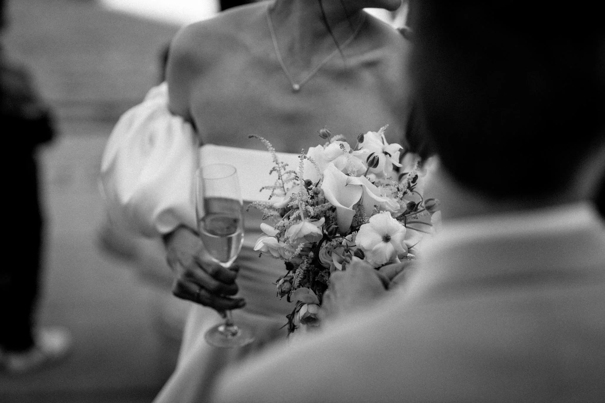 En person holder en stor bouquet af hvide blomster, mens to vinglas står på bordet.