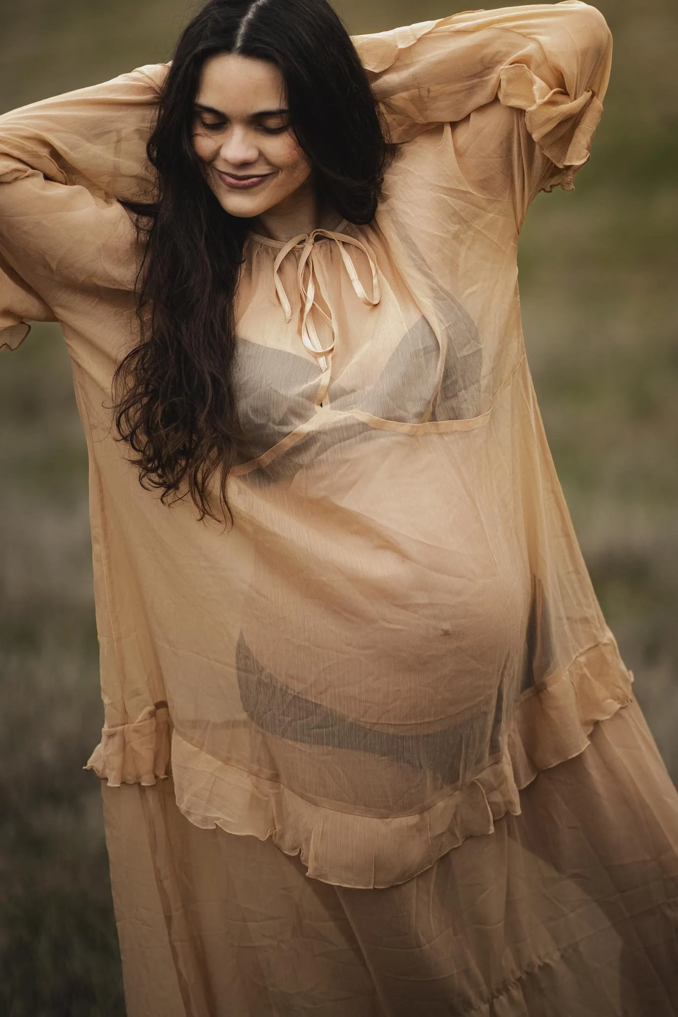 Kvinde iført en løs, lysædelangt kjole med chiffon-lignende stof, der har rynkede detaljer og lange ærmer, taget i et udendørsmiljø.