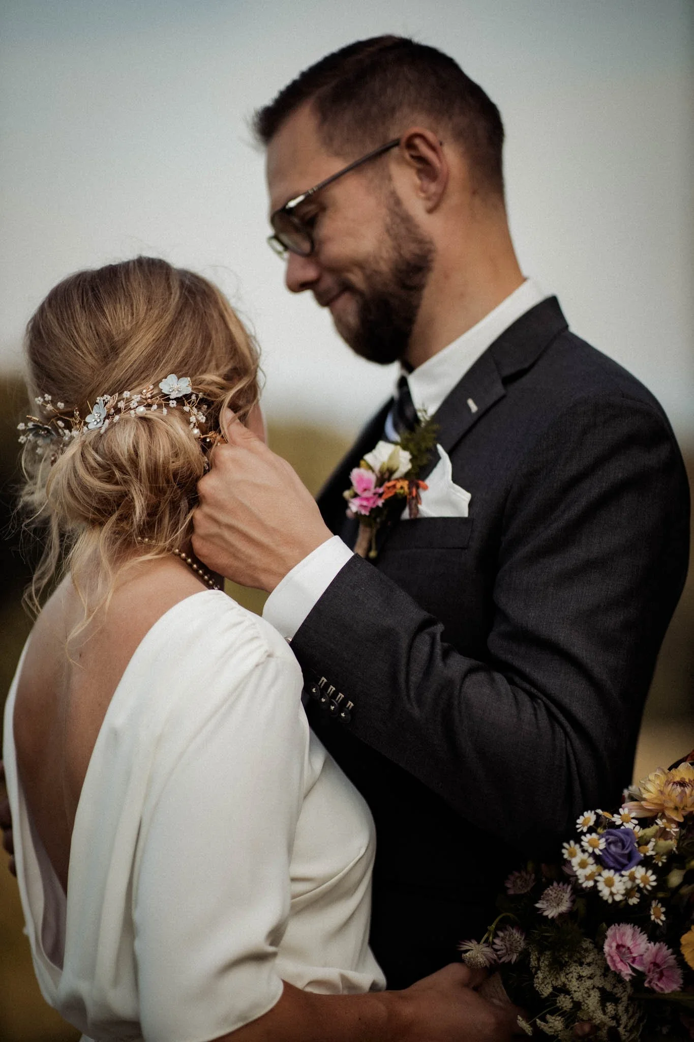 Et bryllupspar danser, kvinden har blond, krøllet hår med en blomsterdekoration. Manden har mørkt hår, skæg og bærer en sort jakkesæt med cylinderkrave. Kvinden holder en stor buket blomster.