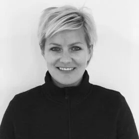 Sort-hvid foto af en smilende kvinde med kort, blondt hårlag, iført sort trøje.