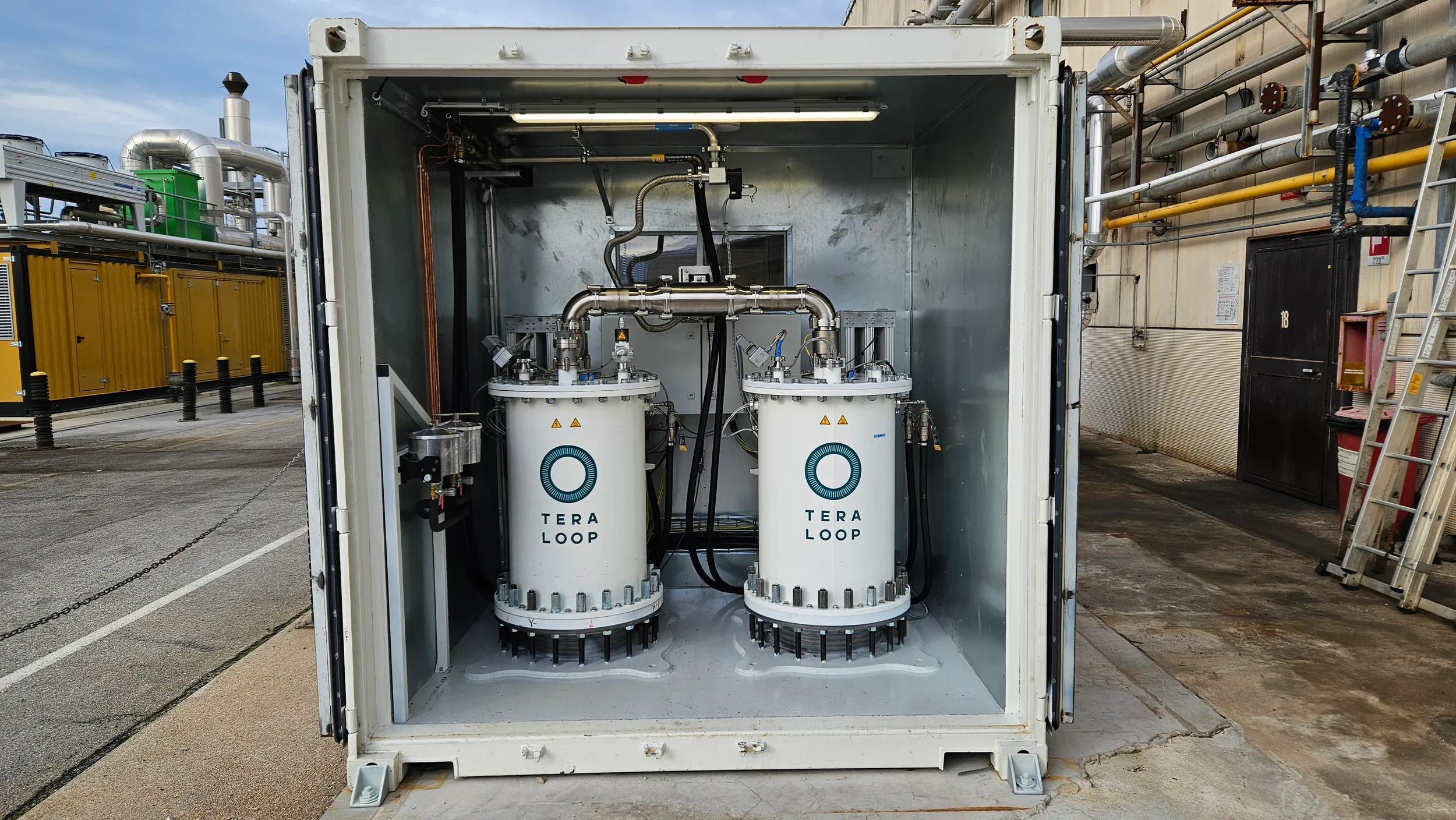 Industrial equipment inside a container labeled 'TERA LOOP' with pipes and machinery, outdoors in an industrial area.