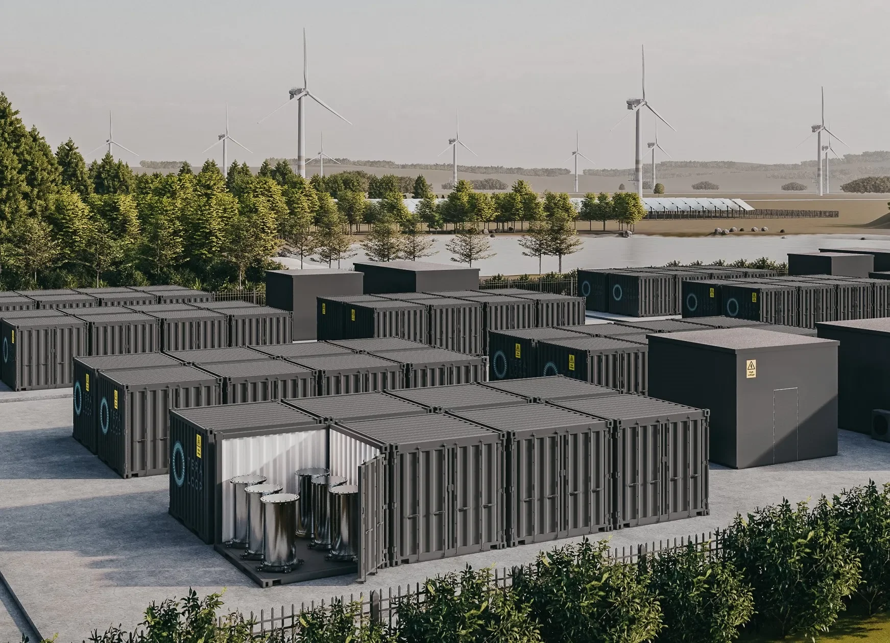 A large outdoor area with numerous black shipping containers, wind turbines in the distance, and a lake or pond surrounded by trees.