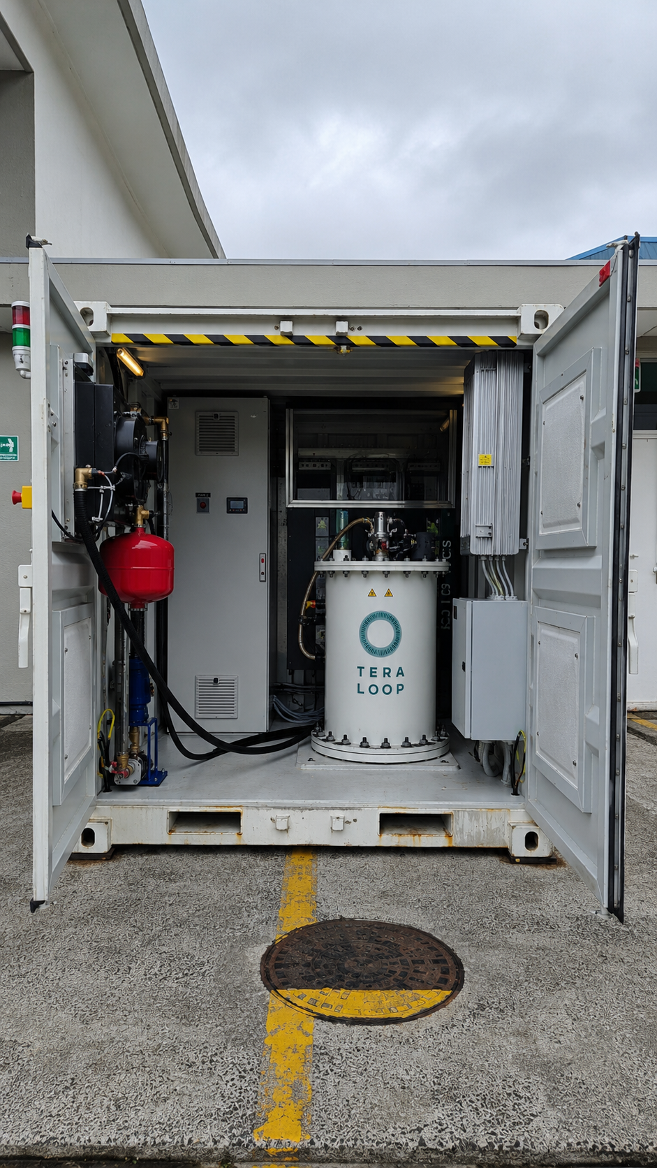 Enclosed container with industrial equipment labeled 'TERA LOOP,' including a white cylindrical tank, electronic controls, pipes, and a red pressure vessel, situated outdoors on a parking lot surface.