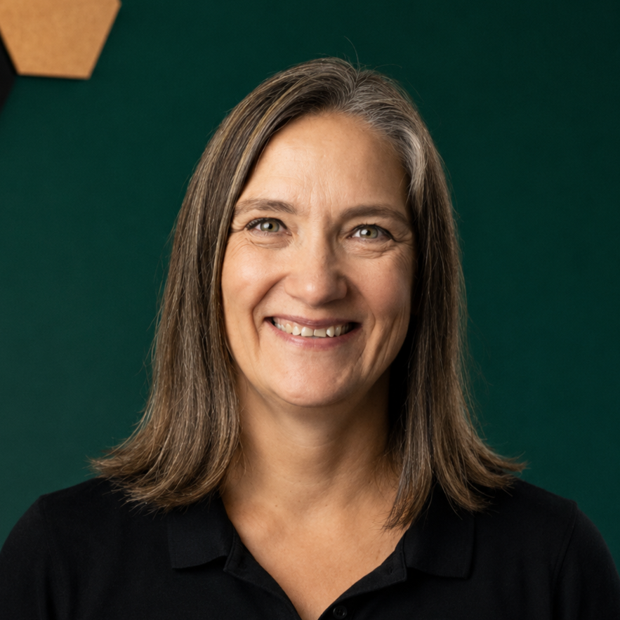 Smiling woman with shoulder-length brown hair wearing a black shirt, standing against a green background.