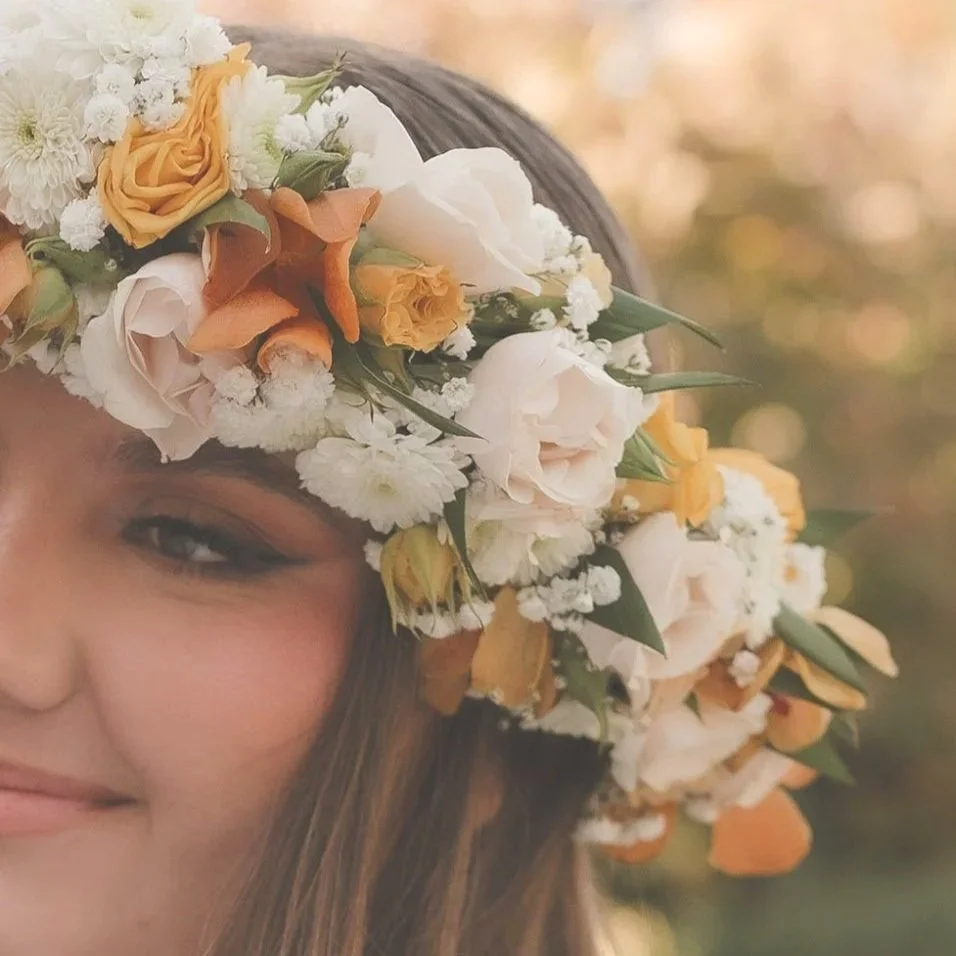 Close-up of a woman wearing a flower crown with white, yellow, and orange flowers.