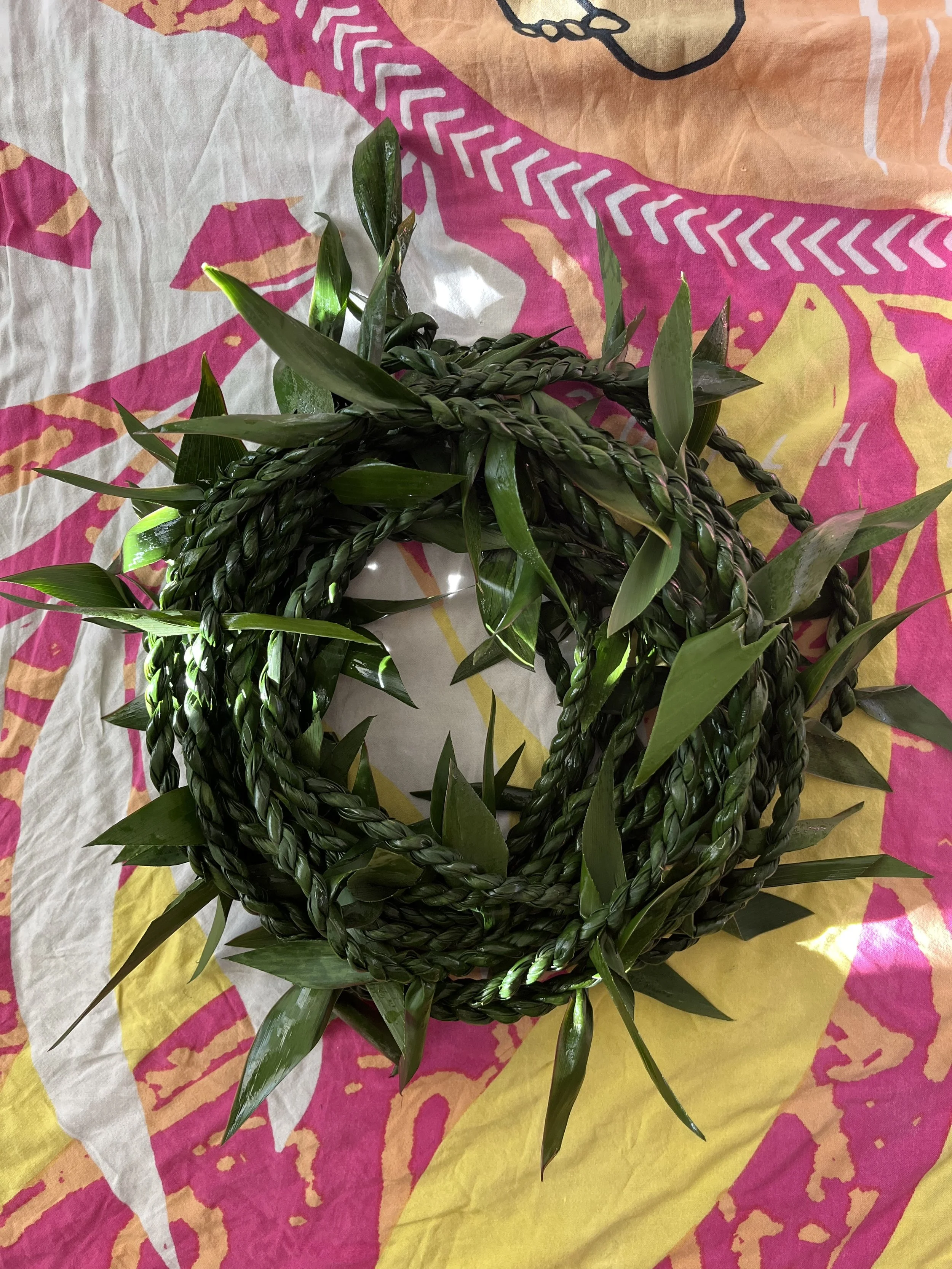 A green braided plant ring placed on a colorful cloth with pink, yellow, and orange patterns.