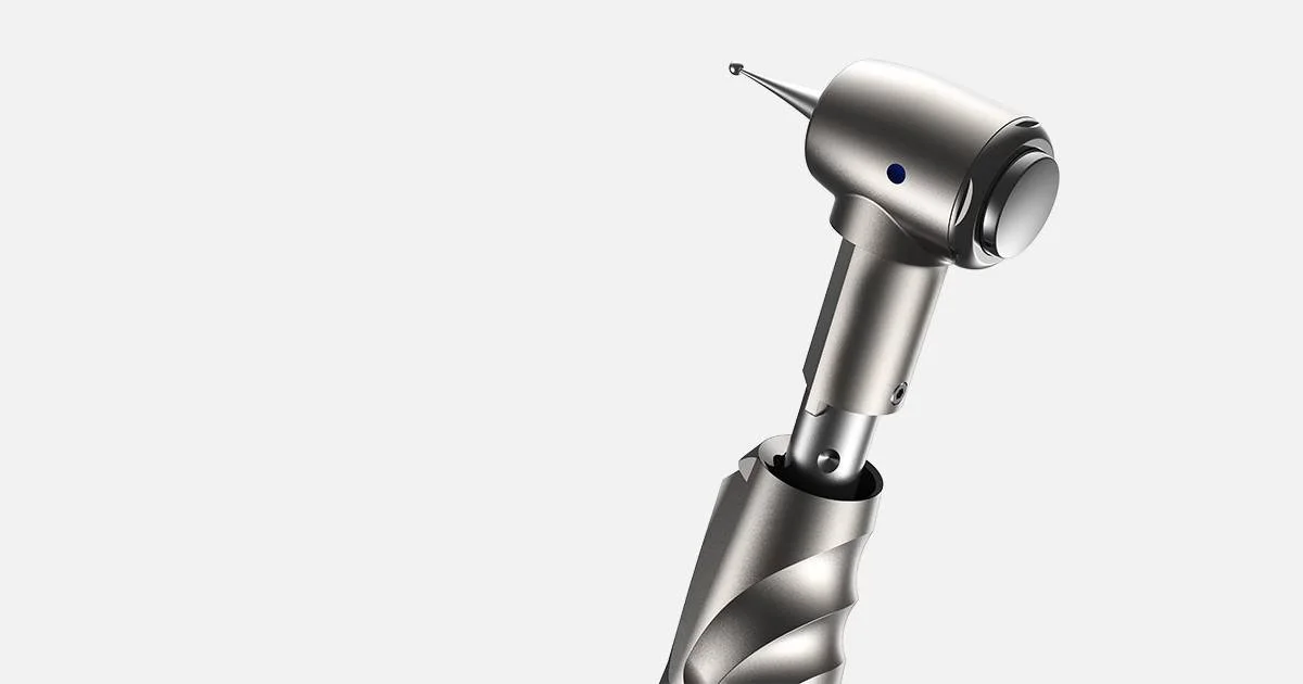 Close-up of a dental surgical handpiece with a pointed drill bit, on a plain light gray background.