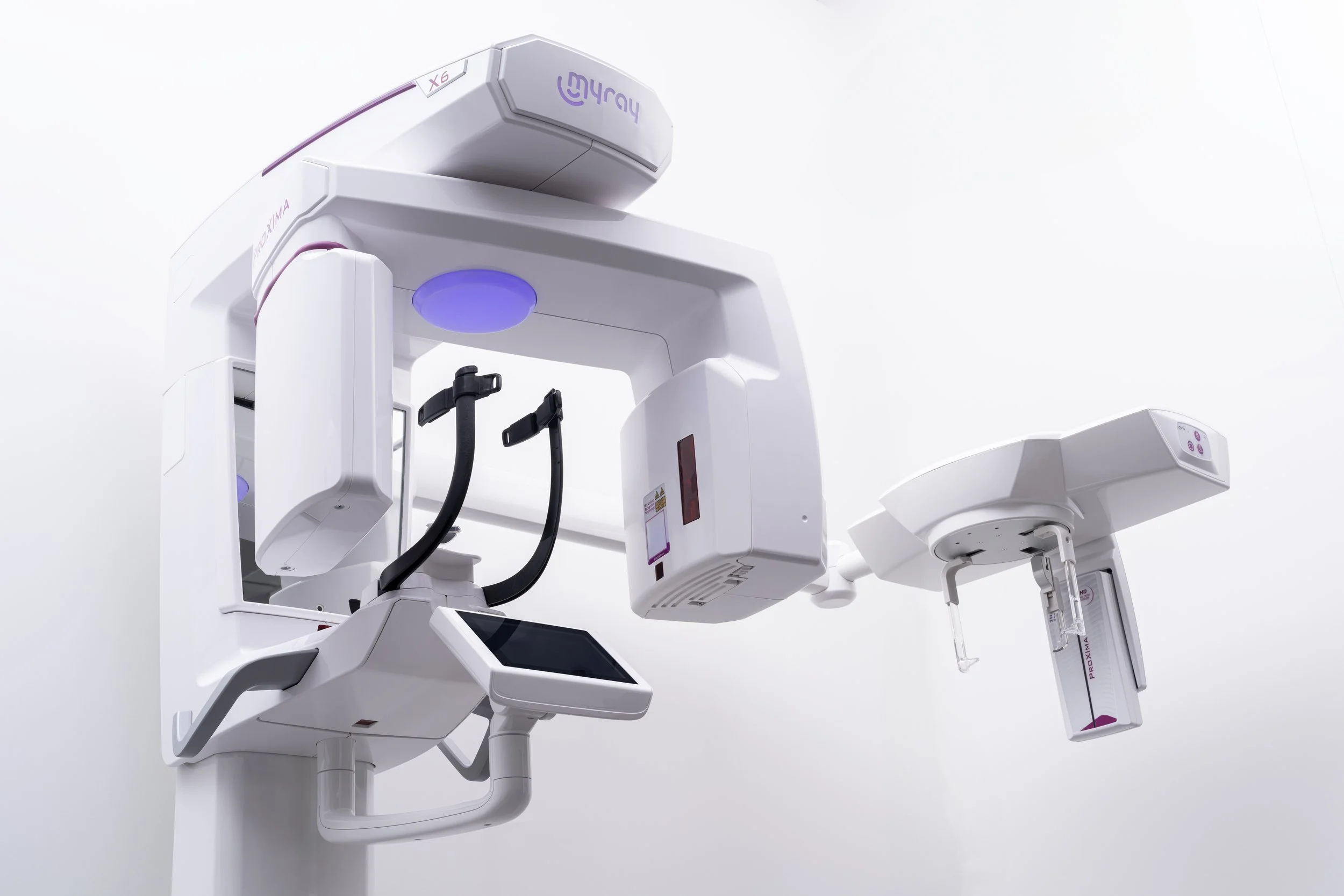 A modern medical imaging machine, likely a CT scanner, with a white structure, black accents, and purple lighting, set against a plain white background.