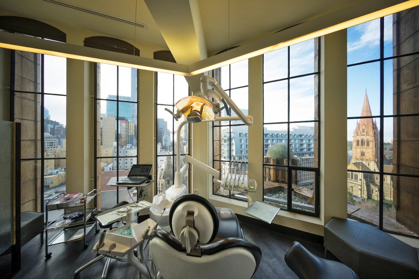 Modern dental office with dental chair, overhead light, computer, and large window view of city skyline and historic church