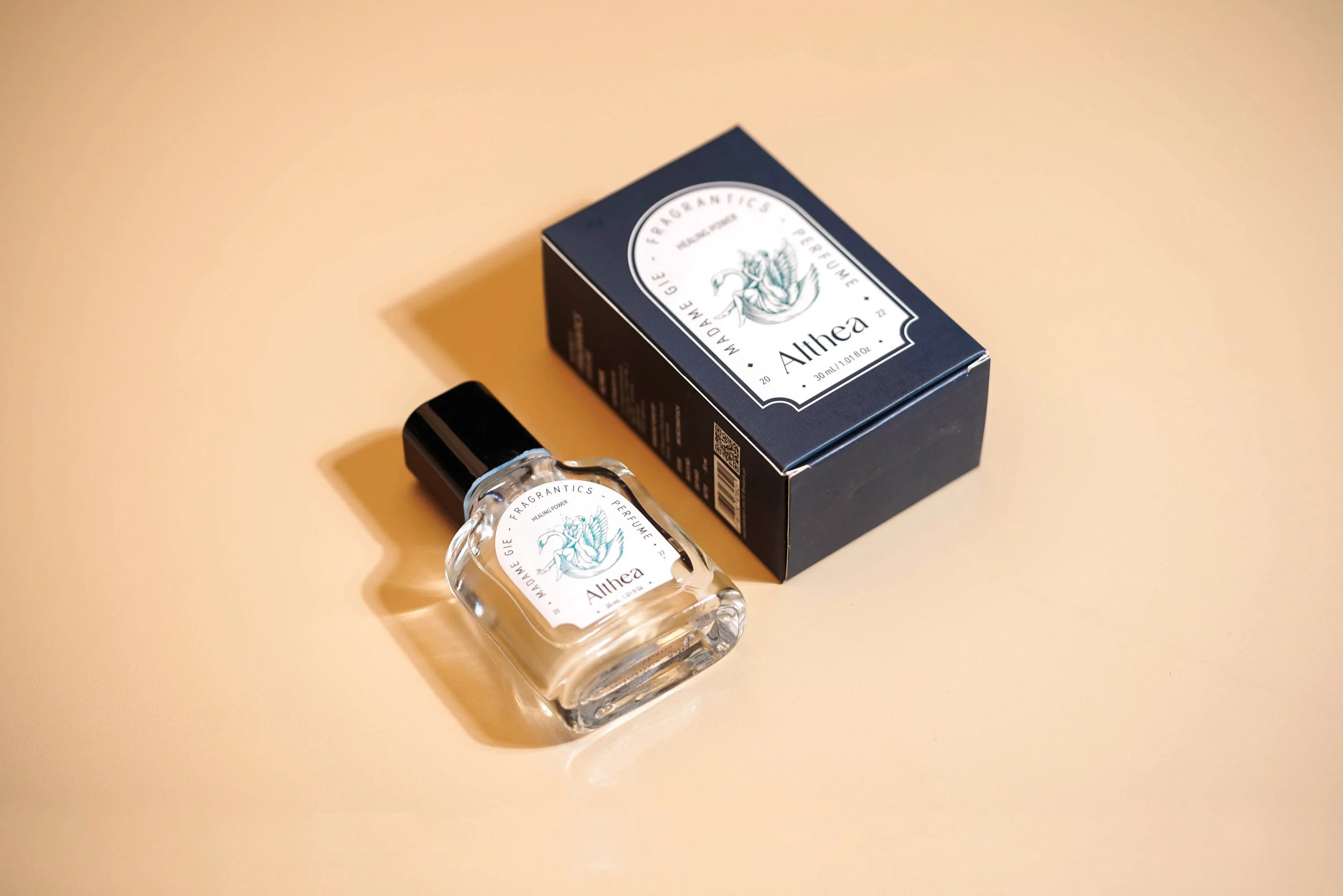 A Madame Gie fragrance bottle resting next to its dark blue textured outer retail packaging box