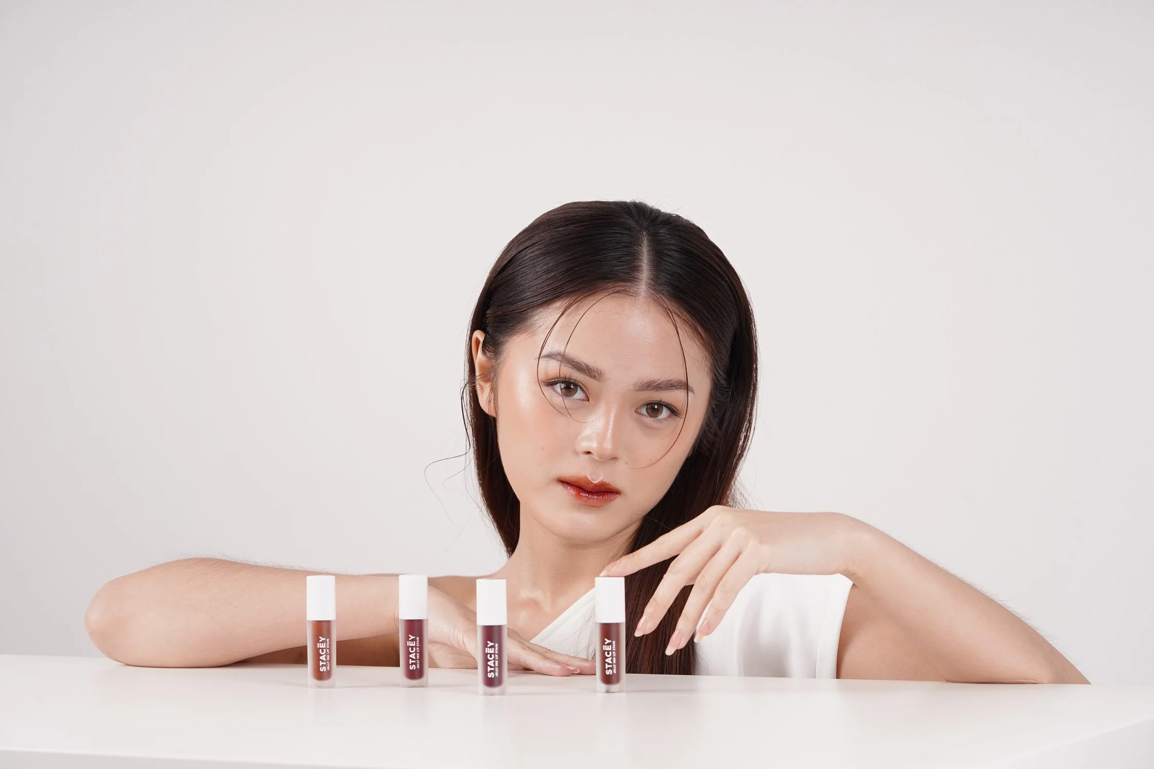 A female model posing behind three small STACEY cosmetic containers lined up on a surface