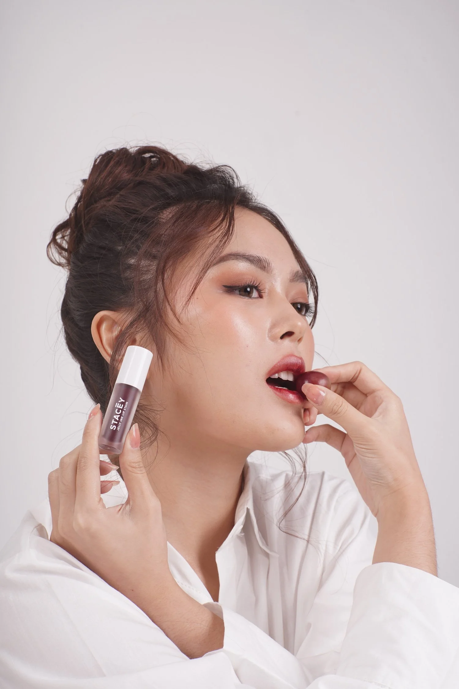 A close-up lifestyle shot of a female model applying a STACEY lip cream product