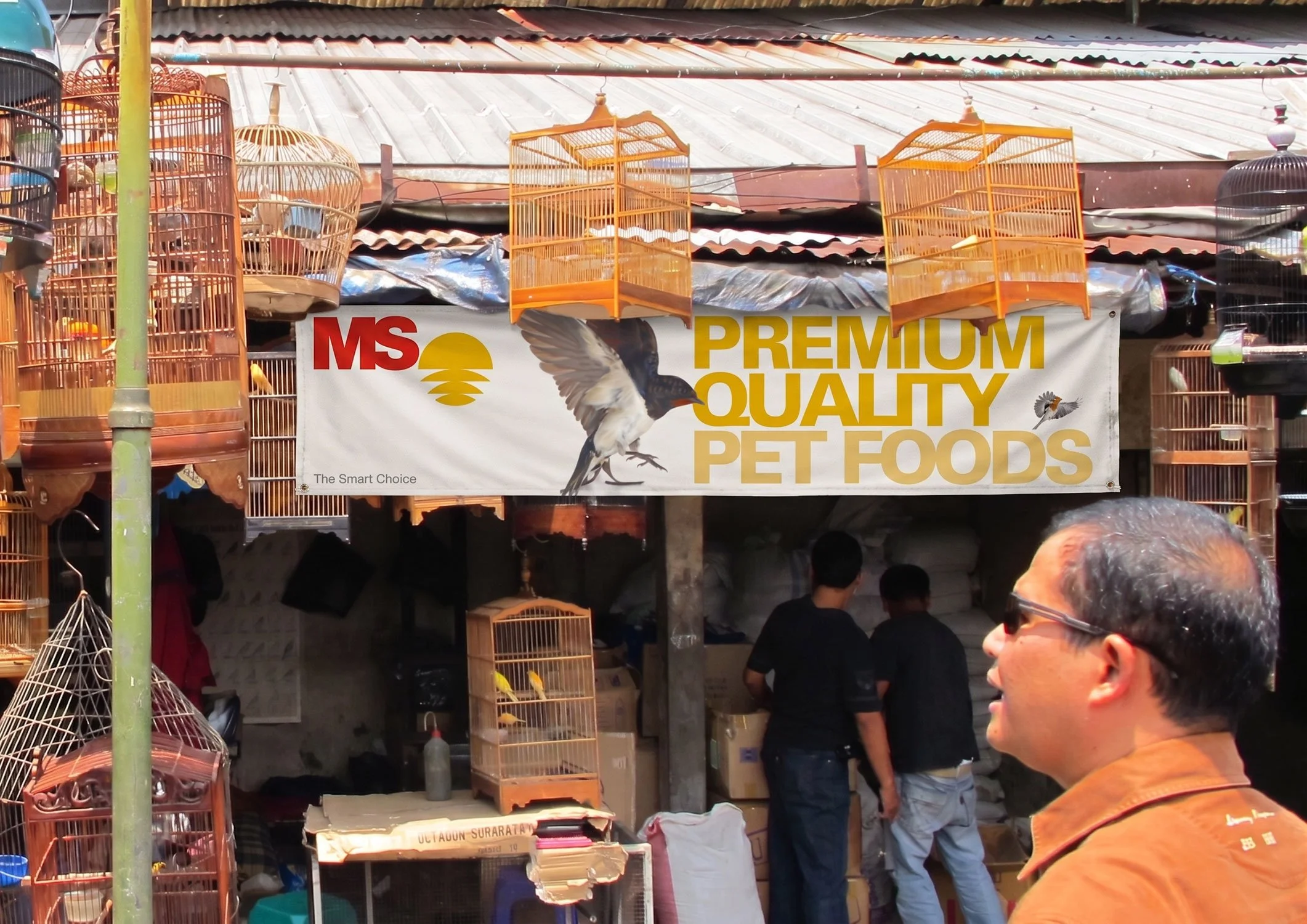 An MS Premium Quality Pet Foods outdoor banner signage hung at a traditional bird and pet market vendor stall