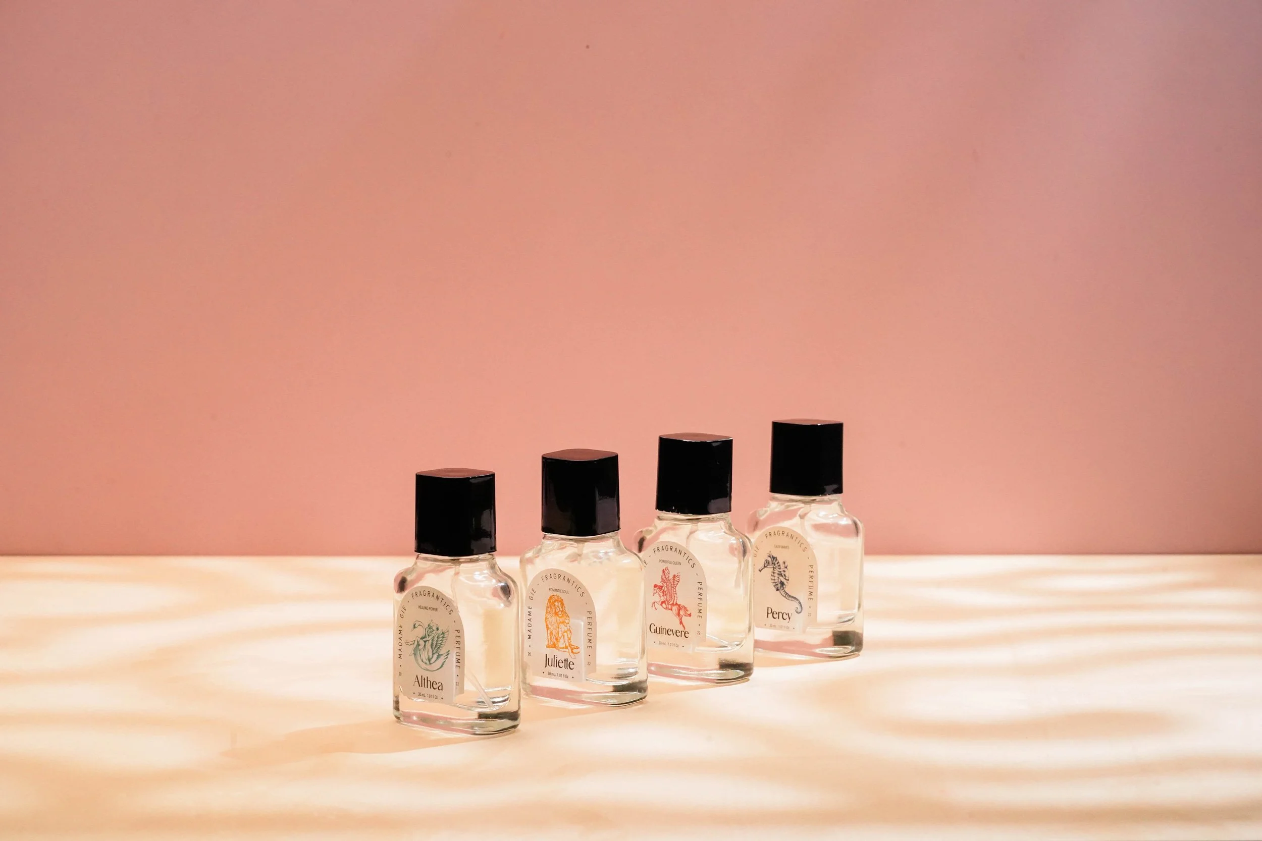A lineup of four different Madame Gie glass perfume variants cast under soft shadows on a warm pastel background