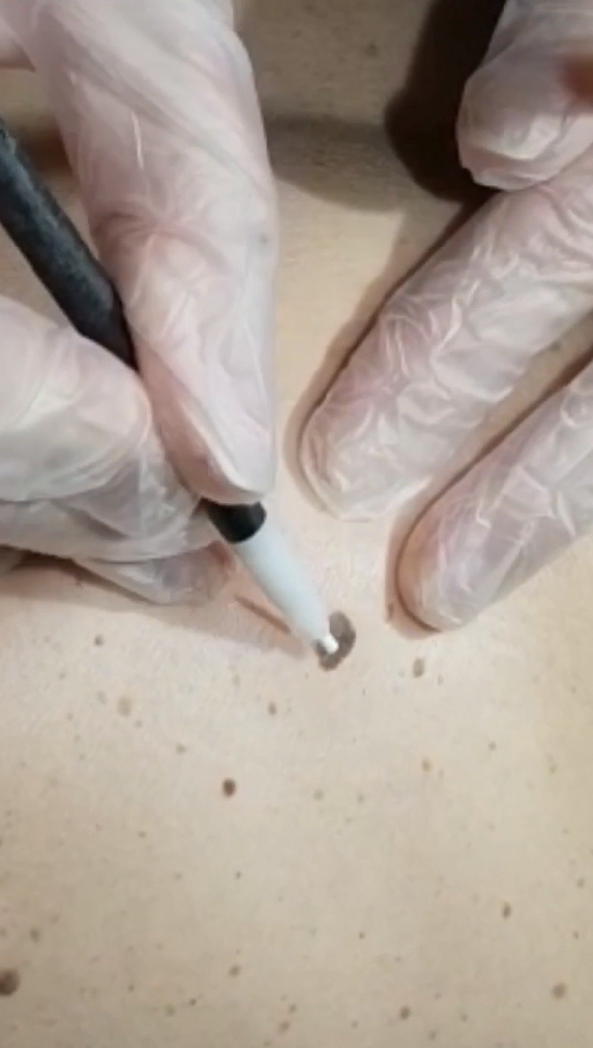 Person wearing plastic gloves writing or drawing with a black marker on a light-colored surface.