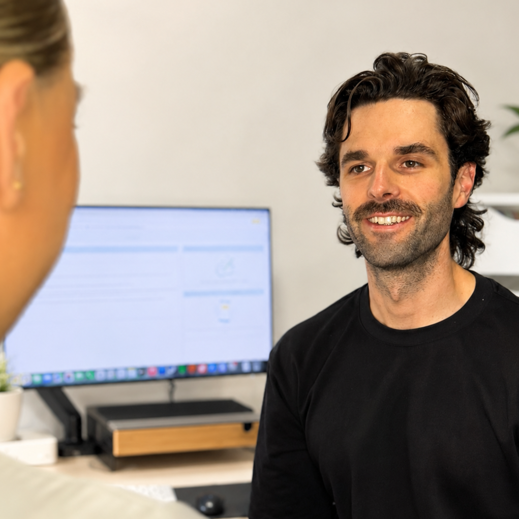A man with dark, wavy hair and a beard smiling during a conversation in an office.