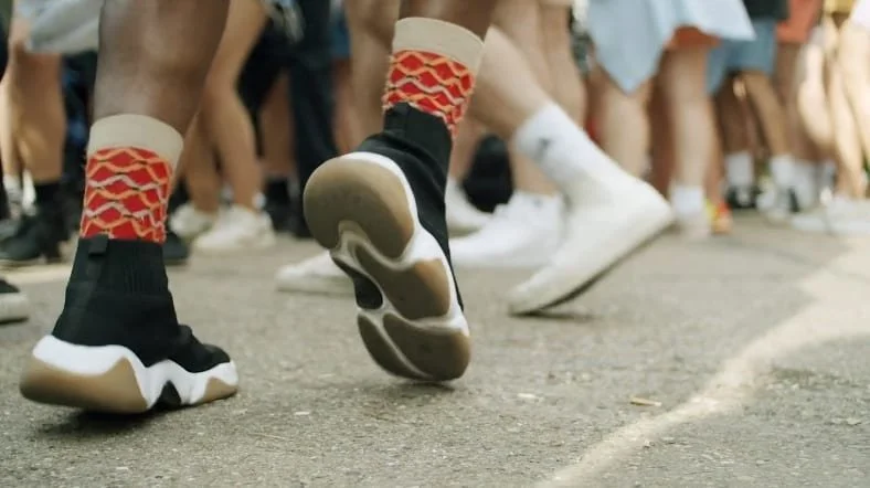 Close-up of a runner's shoes and legs during a race on a street, with other runners in the background.