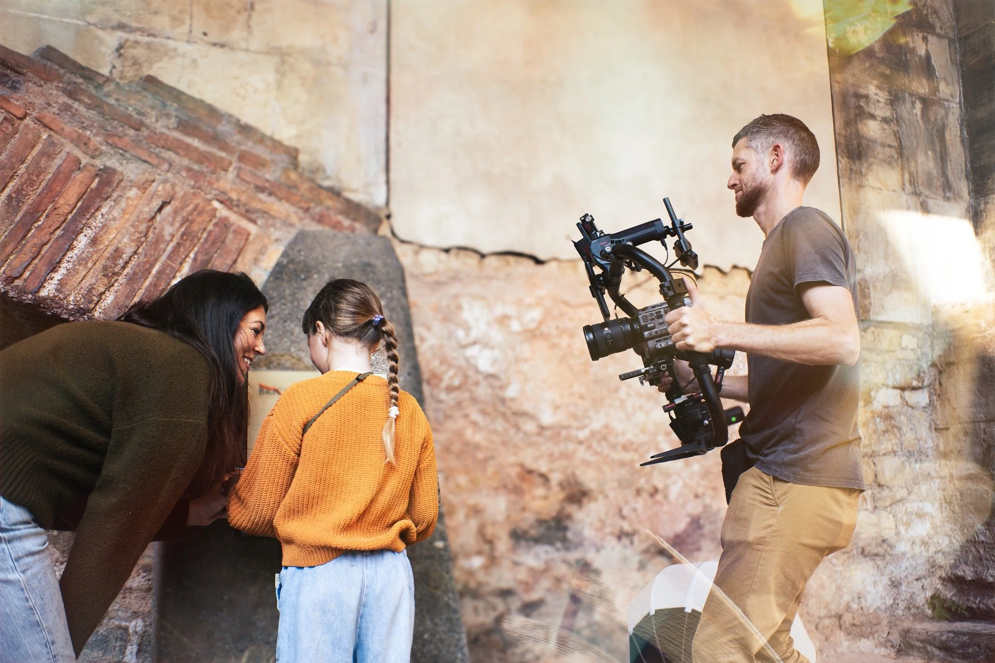 Filmmaker recording a woman and girl looking at a plaque on a stone wall