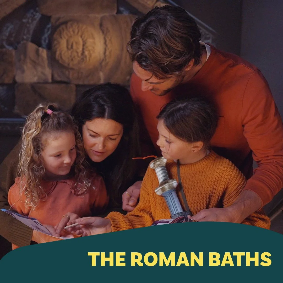 A family of four, including two children, looking at a tablet and holding a toy sword, gathered around together in a cozy room with a stone fireplace.