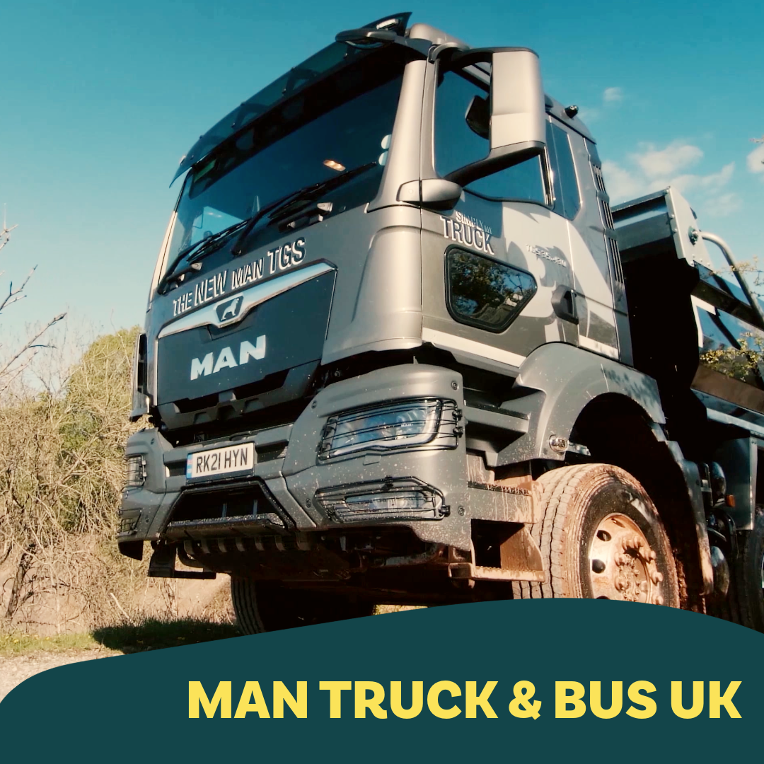 A large MAN truck parked outdoors with a clear sky background. The truck is gray with black accents, and the text 'The New MAN TGS' is visible on the front. The truck has a visible license plate reading 'RK21 HYN'. The photo is taken from a low angle showing the front and side of the truck.