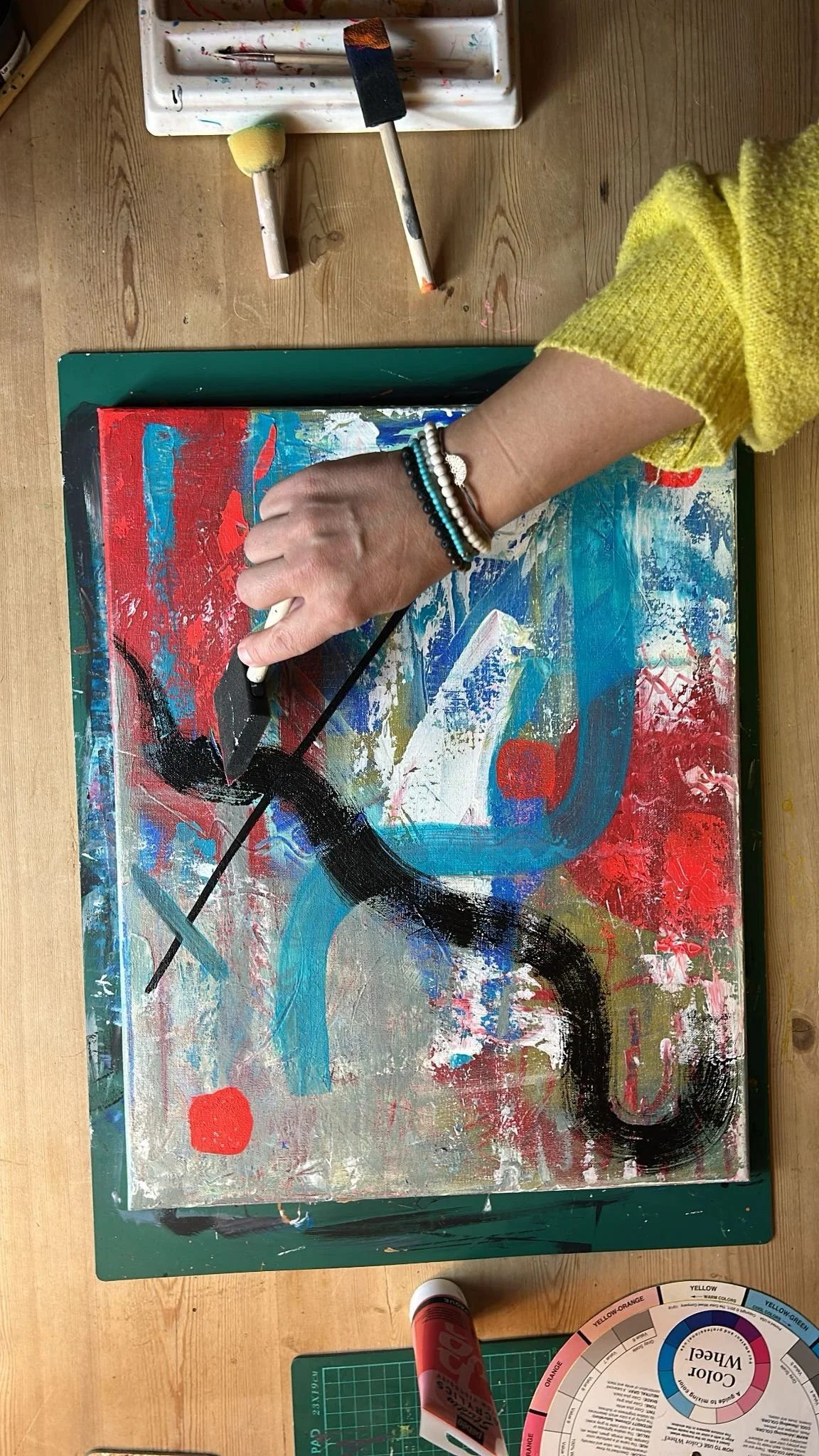 Artist AmyLou Fouillet working on a layered abstract painting with expressive marks and colour.