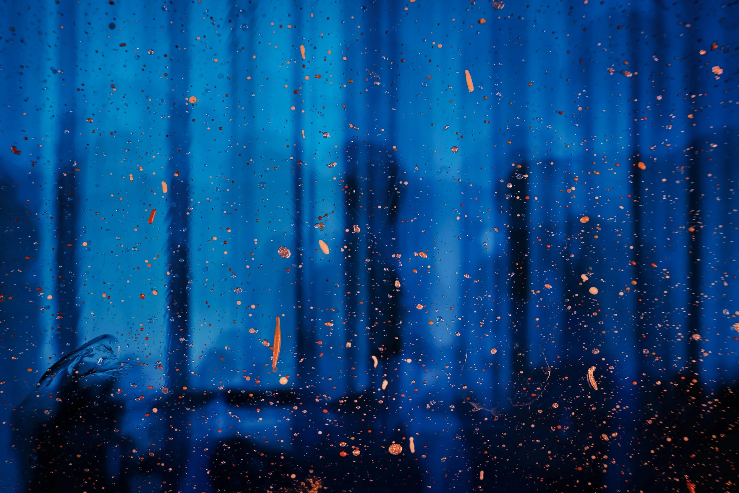 Close-up of a blue surface with many orange and brown paint splatters and drips, some areas showing a darker, shadowed background.