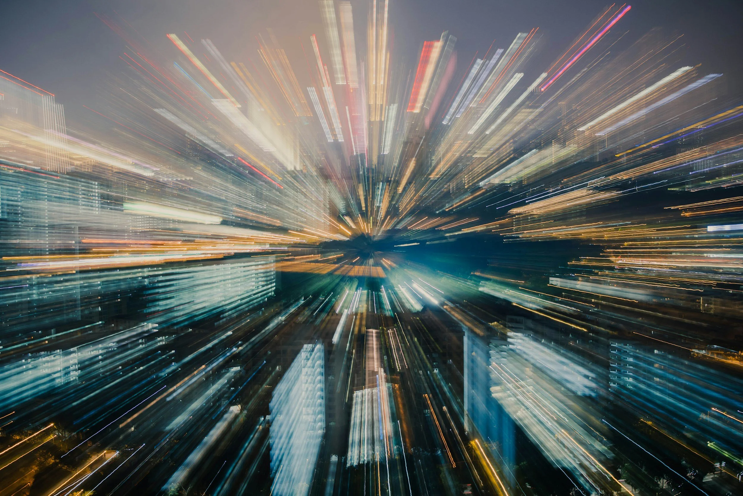 Long exposure photo of a city at night with streaks of colorful lights from moving vehicles and buildings.