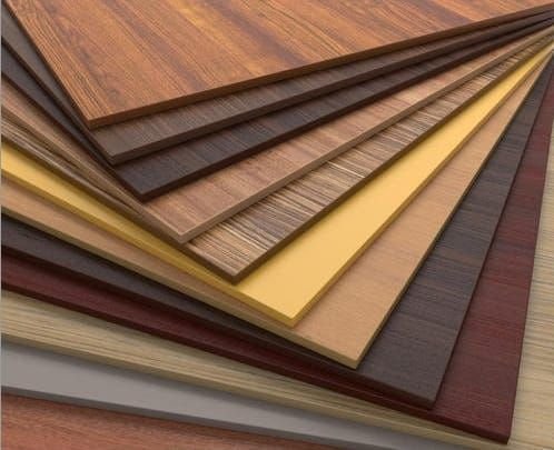 Stacked sheets of various wood grain and color laminate or veneer materials.