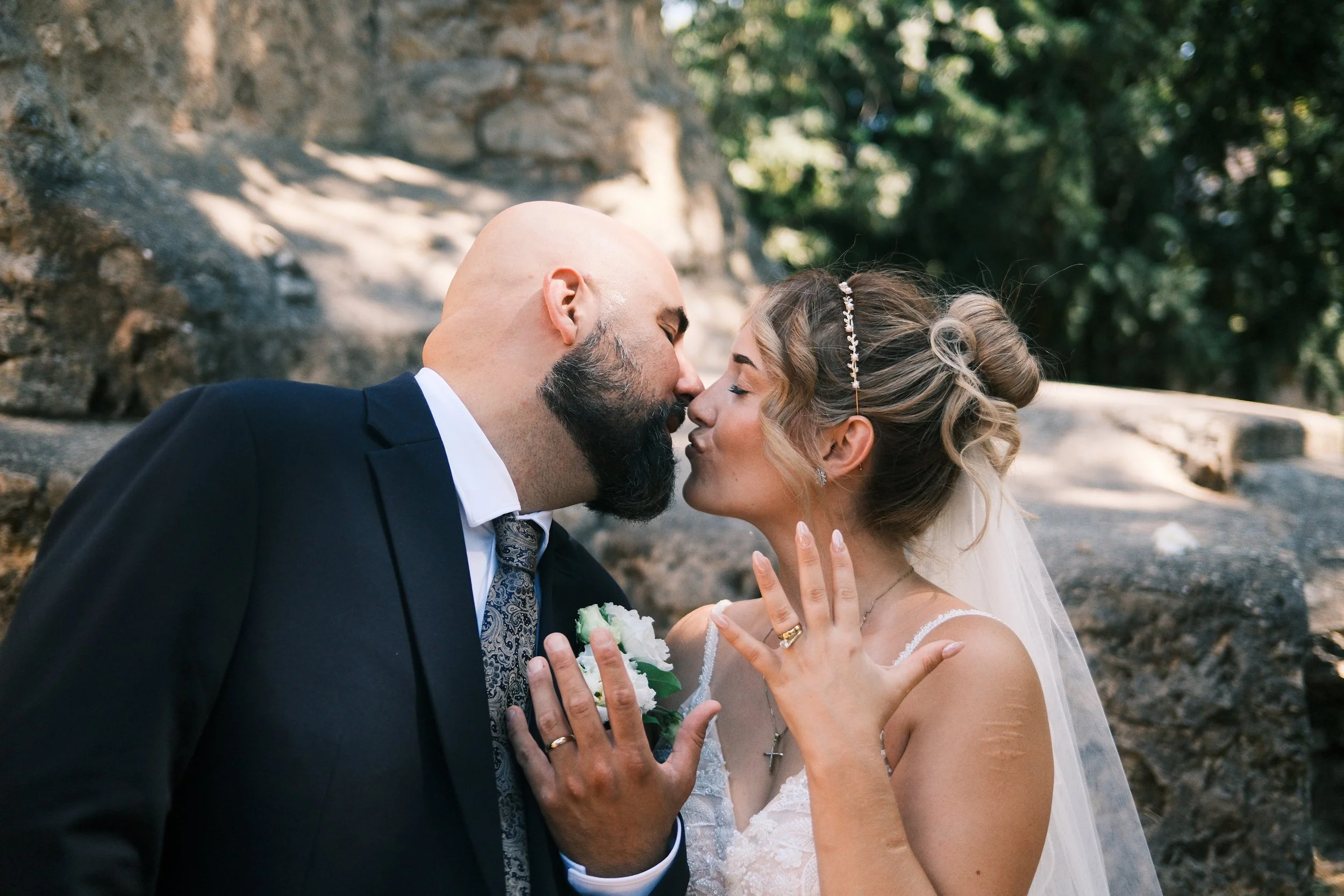 Brautpaar küsst sich vor einer Natursteinmauer, Braut zeigt lachend ihren Ehering, Hochzeit in Leipzig