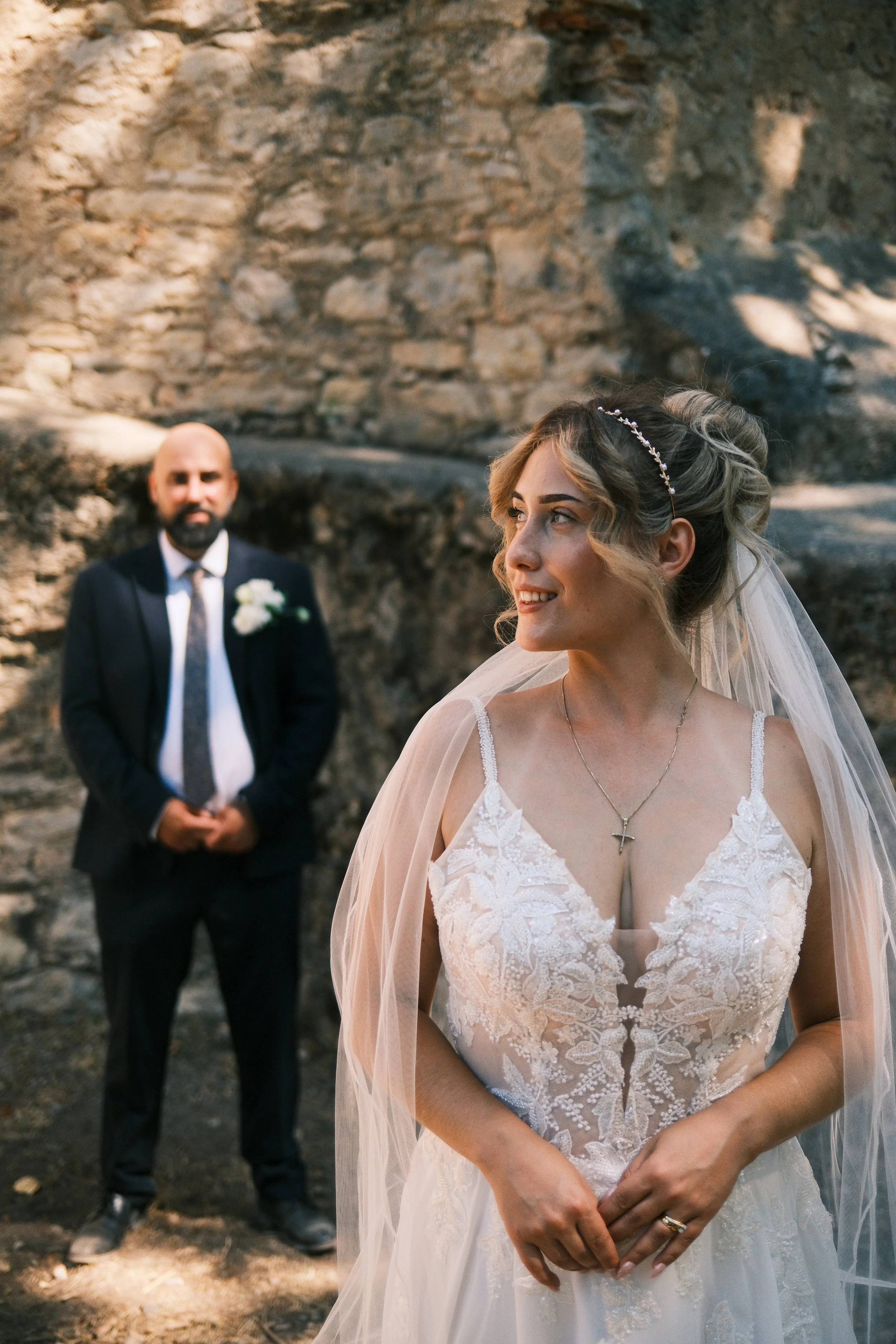 Alt-Text: Braut mit Blumenstrauß blickt vor einer Natursteinmauer über die Schulter zurück, Hochzeit in Leipzig