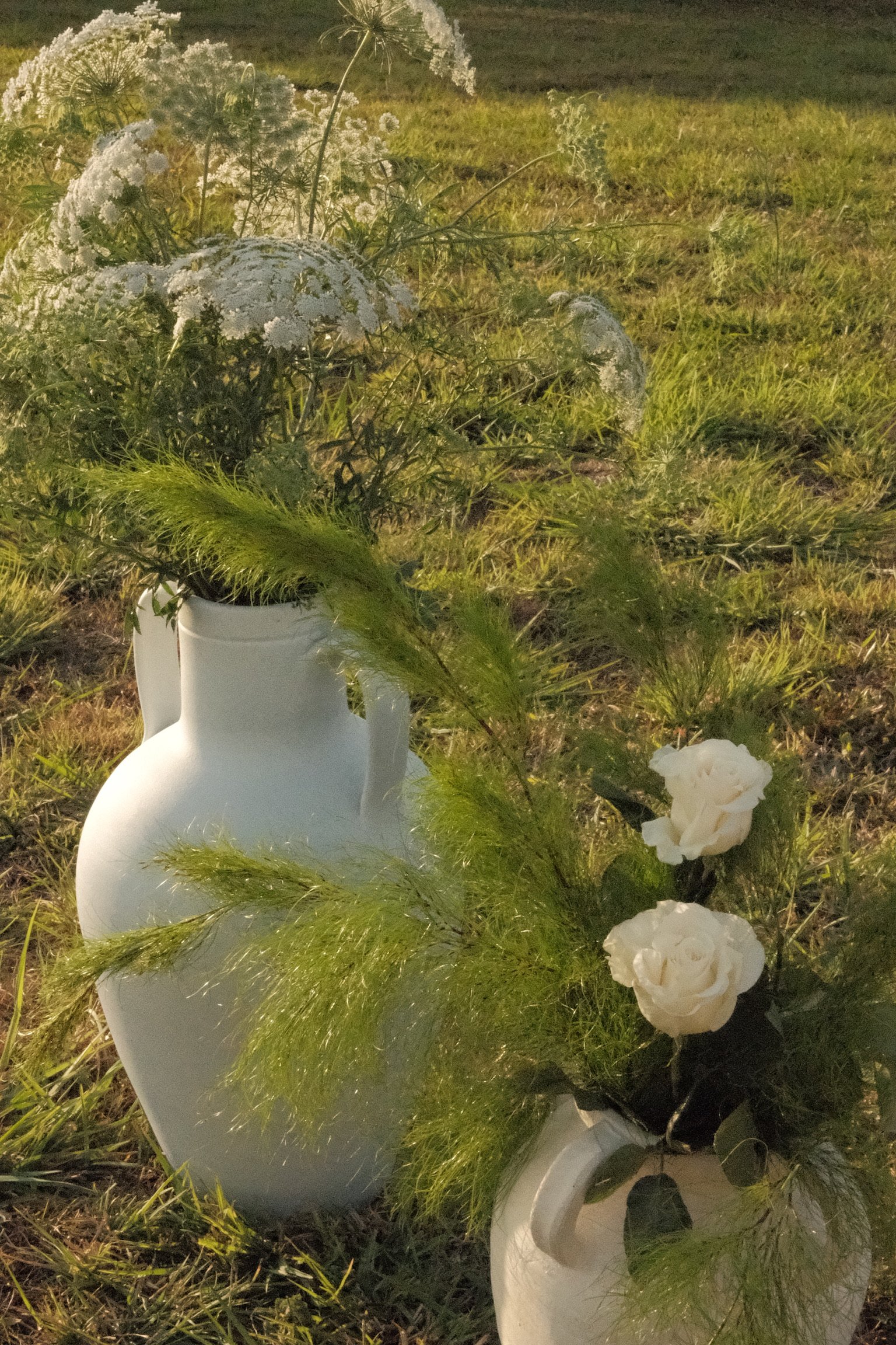 White ceramic swan vases filled with white flowers and green foliage, placed on grass at night.