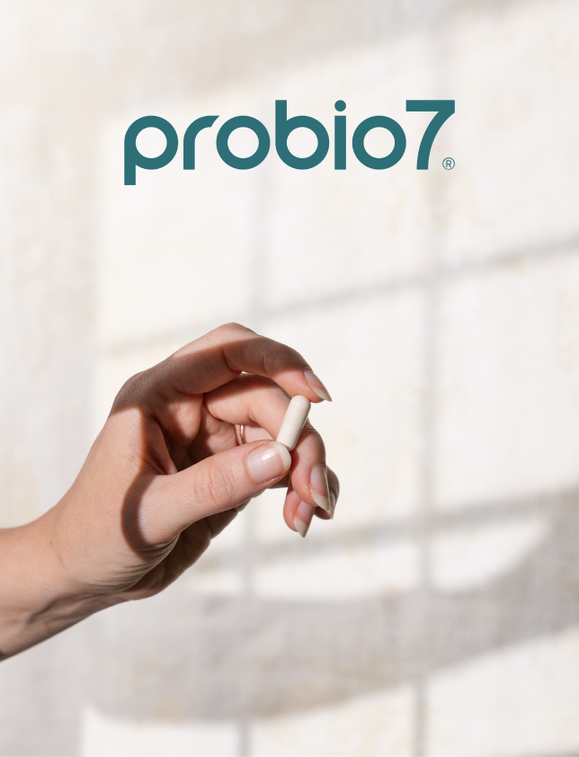 A hand holding a probiotic capsule in front of a wall with the probiotic7 logo.