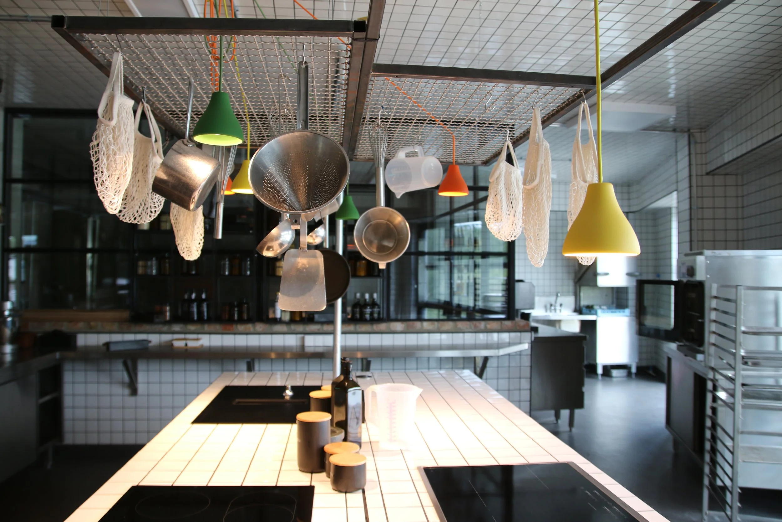 Küche mit weißem Backstein-Esstisch, Hängelampen in Grün, Gelb und Orange, Kochutensilien und Geschirr, moderner Industrielook, background mit Schrank und offene Regale.