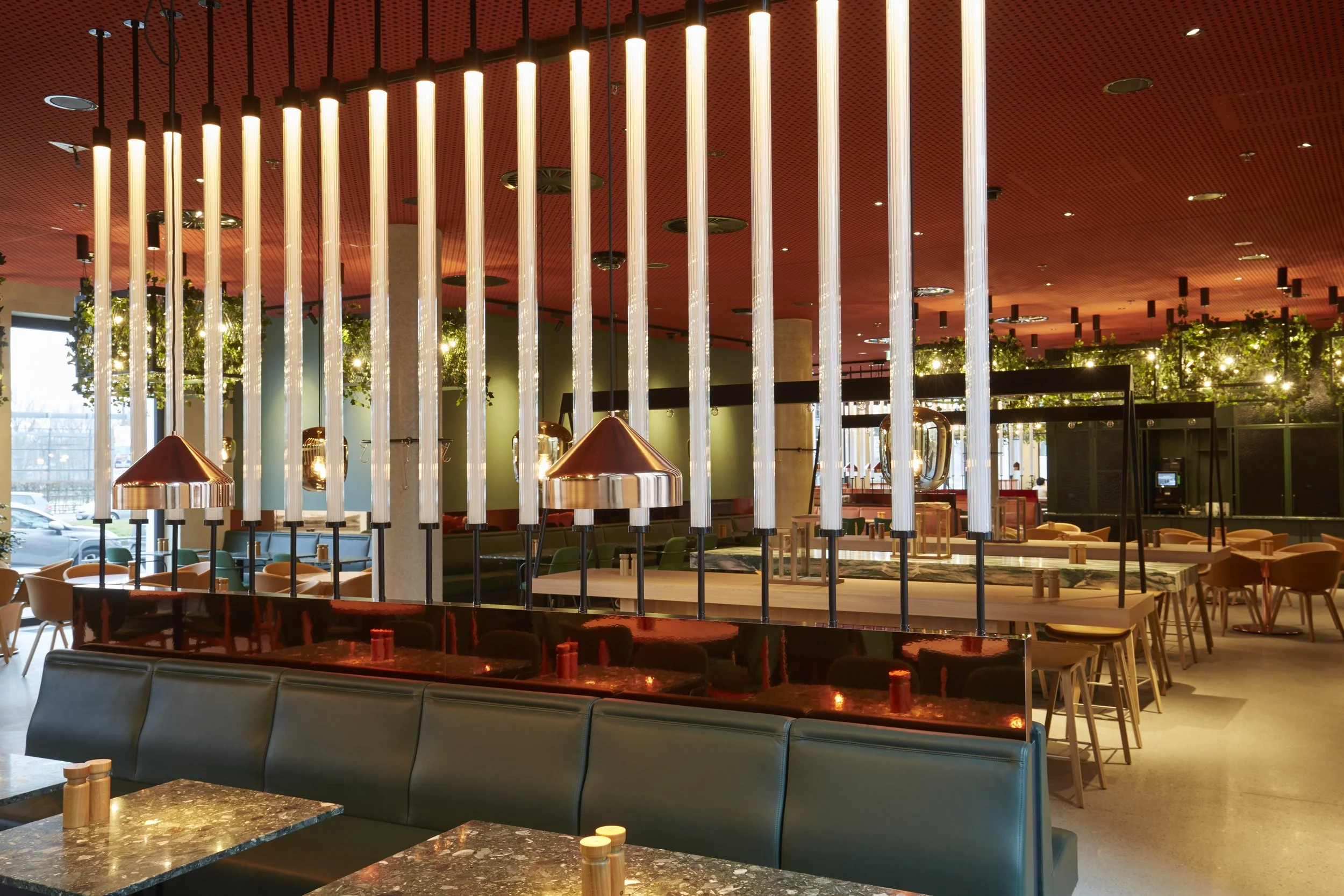 Innenbereich eines modernen Restaurants oder Lounge mit rotem Decke, Lichtelementen, Pflanzen und Sitzmöbeln.