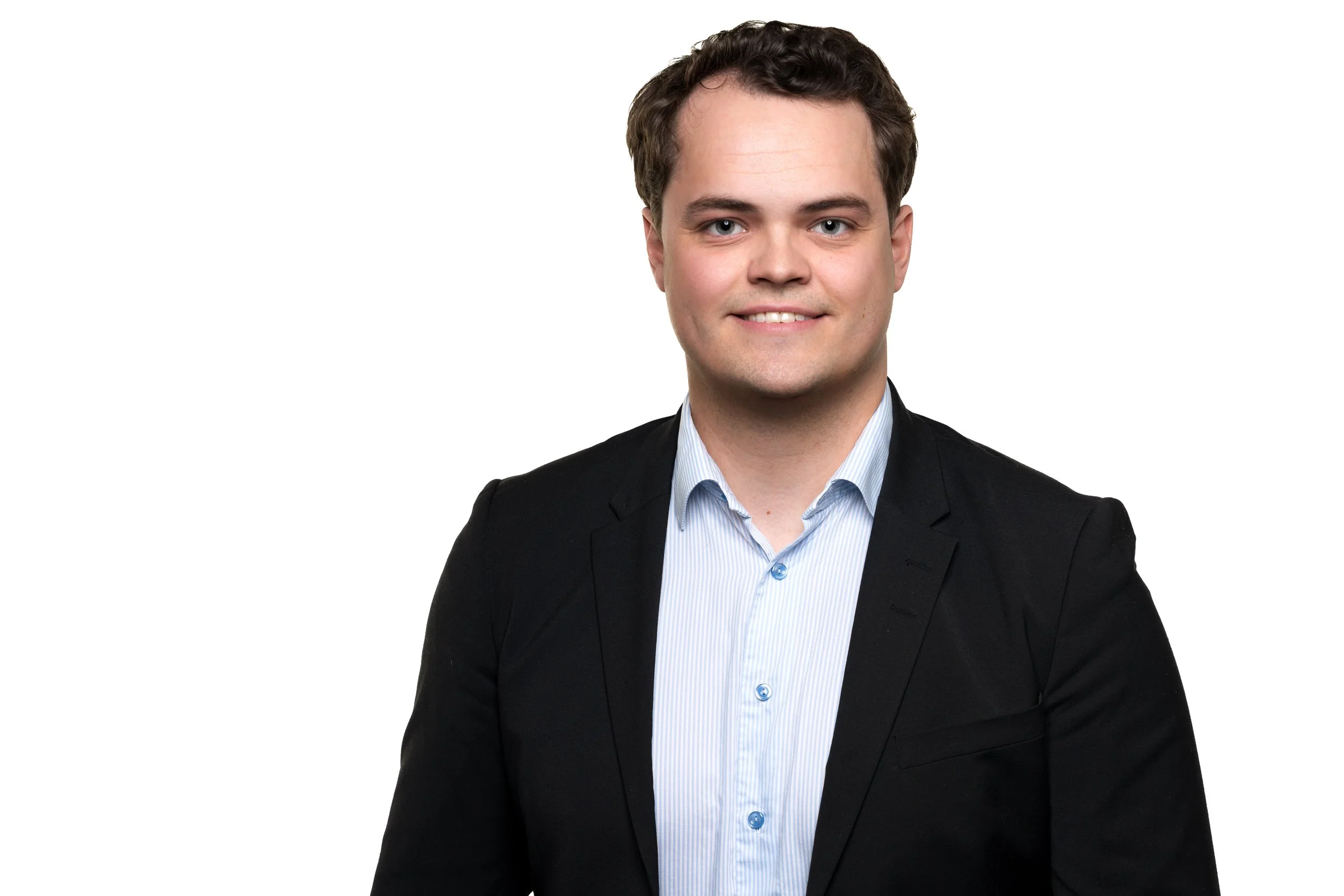 Portrett av en ung mann med mørkt, krøllete hår, iført en svart dress og lys blå skjorte, mot en hvit bakgrunn.