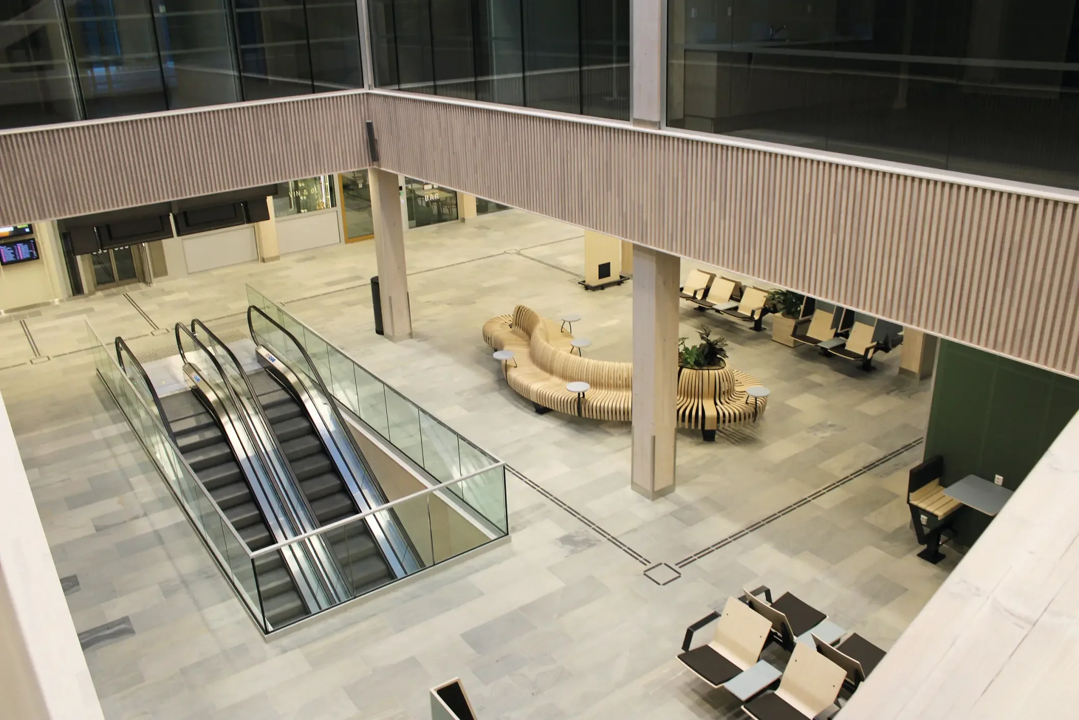 Innendørsområde i et moderne bygg med rulletrapper, sitteområder og store glassvinduer.