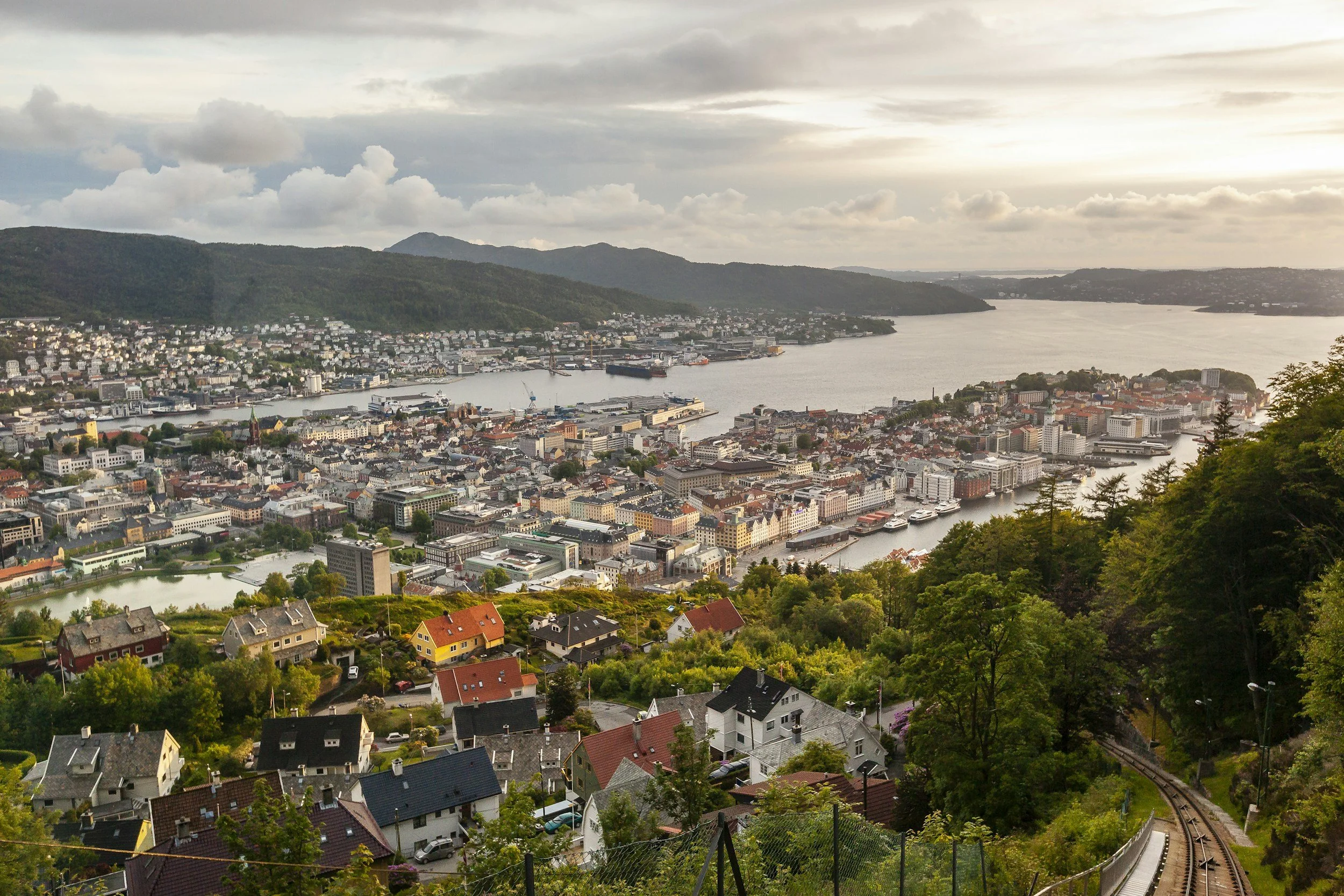 Utsikt over Bergen, en by ved en fjord omgitt av fjell, med hus, bygninger og en jernbanespor.