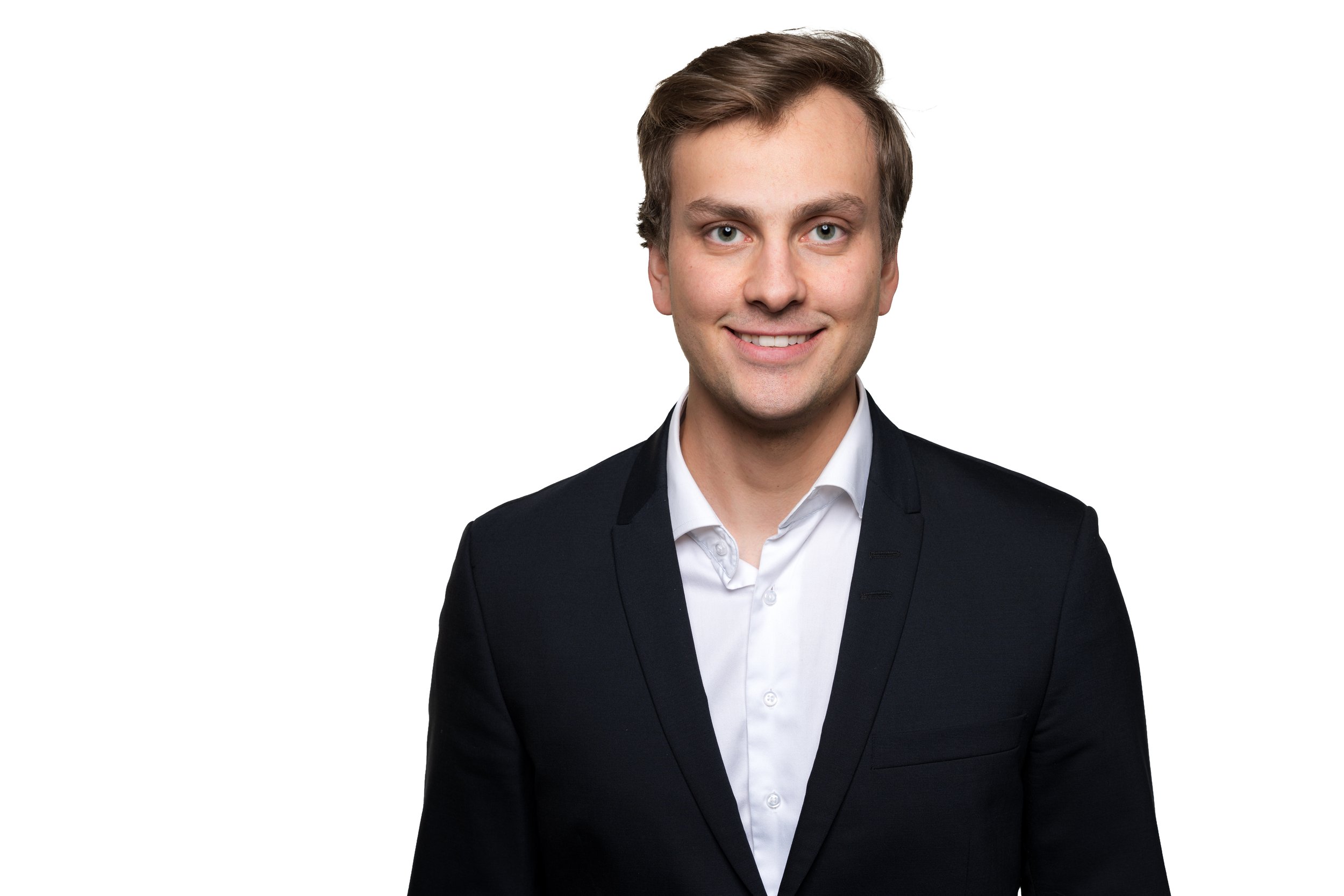 Ung mann i sort dress med hvit skjorte smilende mot kamera, bukser og blixtlås.
