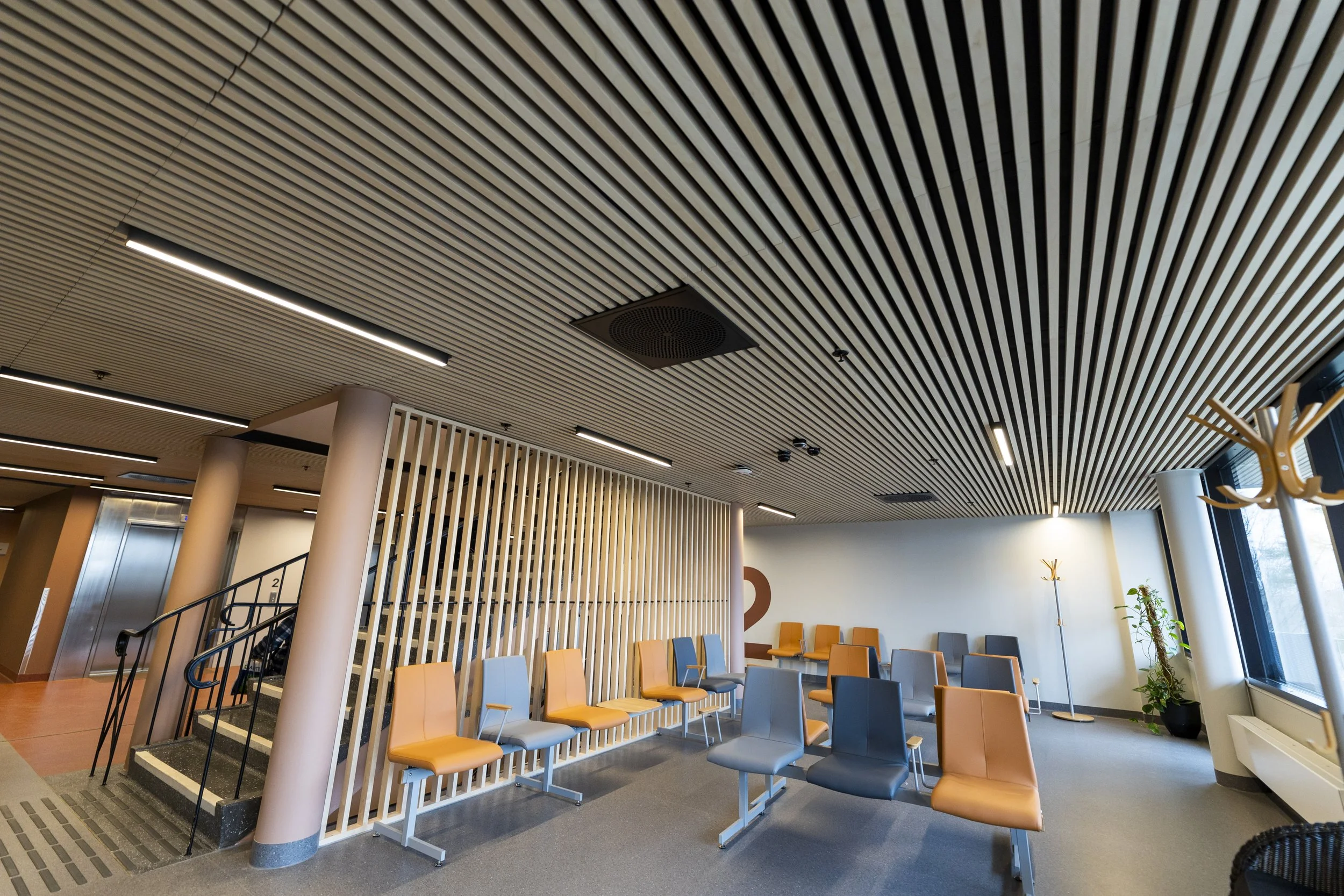 Innendørsventrom i en offentlig bygning, med vanligvis ventestoler i orange og blått. Moderne tak med innebygde lys og ventilasjonsanlegg. Rader med ventestoler plassert langs veggen og en trapp som fører til en annen etasje.