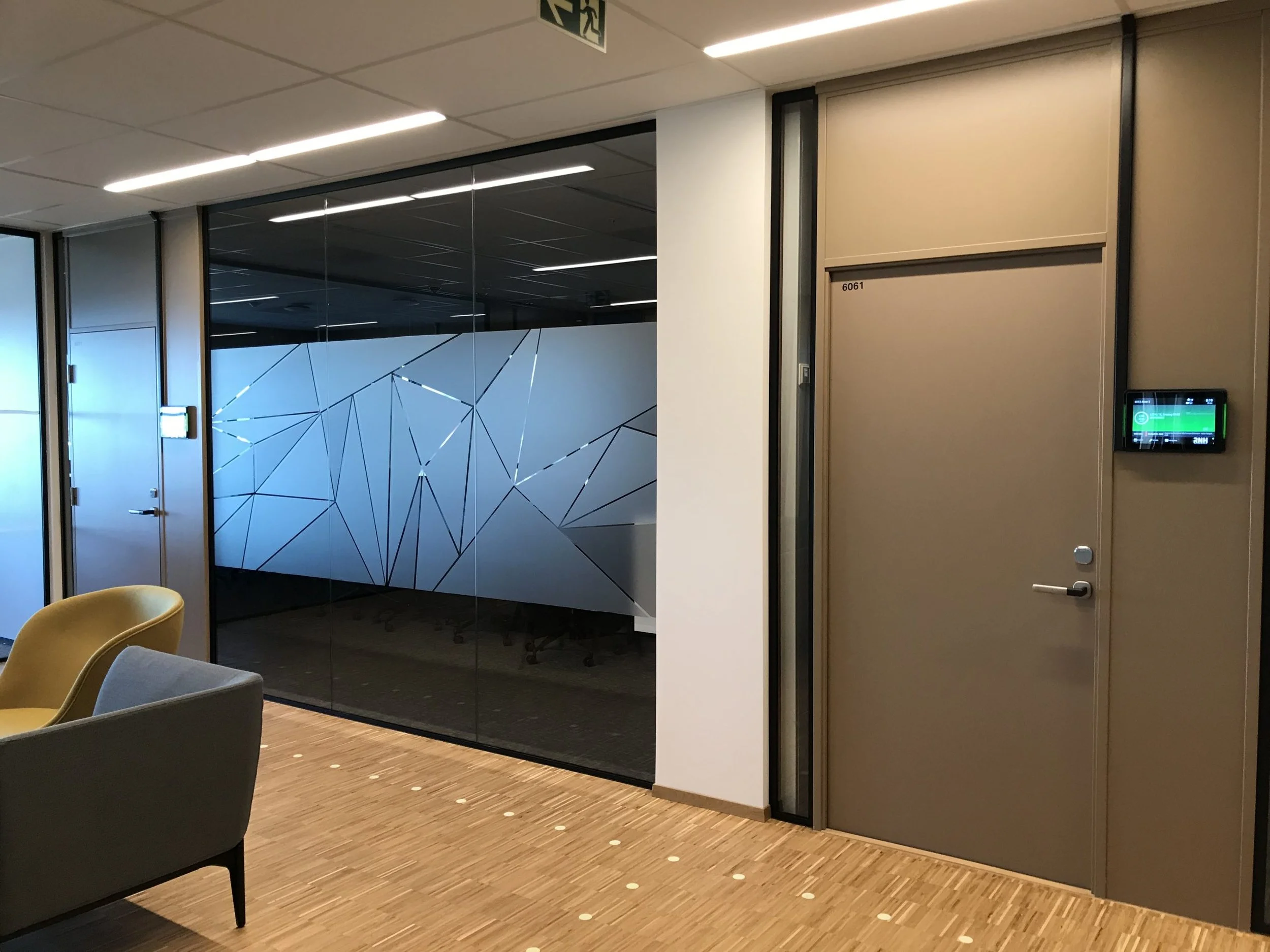 Innvendig bilde av et kontorlokale eller møterom med lenestoler, en glassvegg med geometriske design, og en vegg med en rekke digitale skjermer.