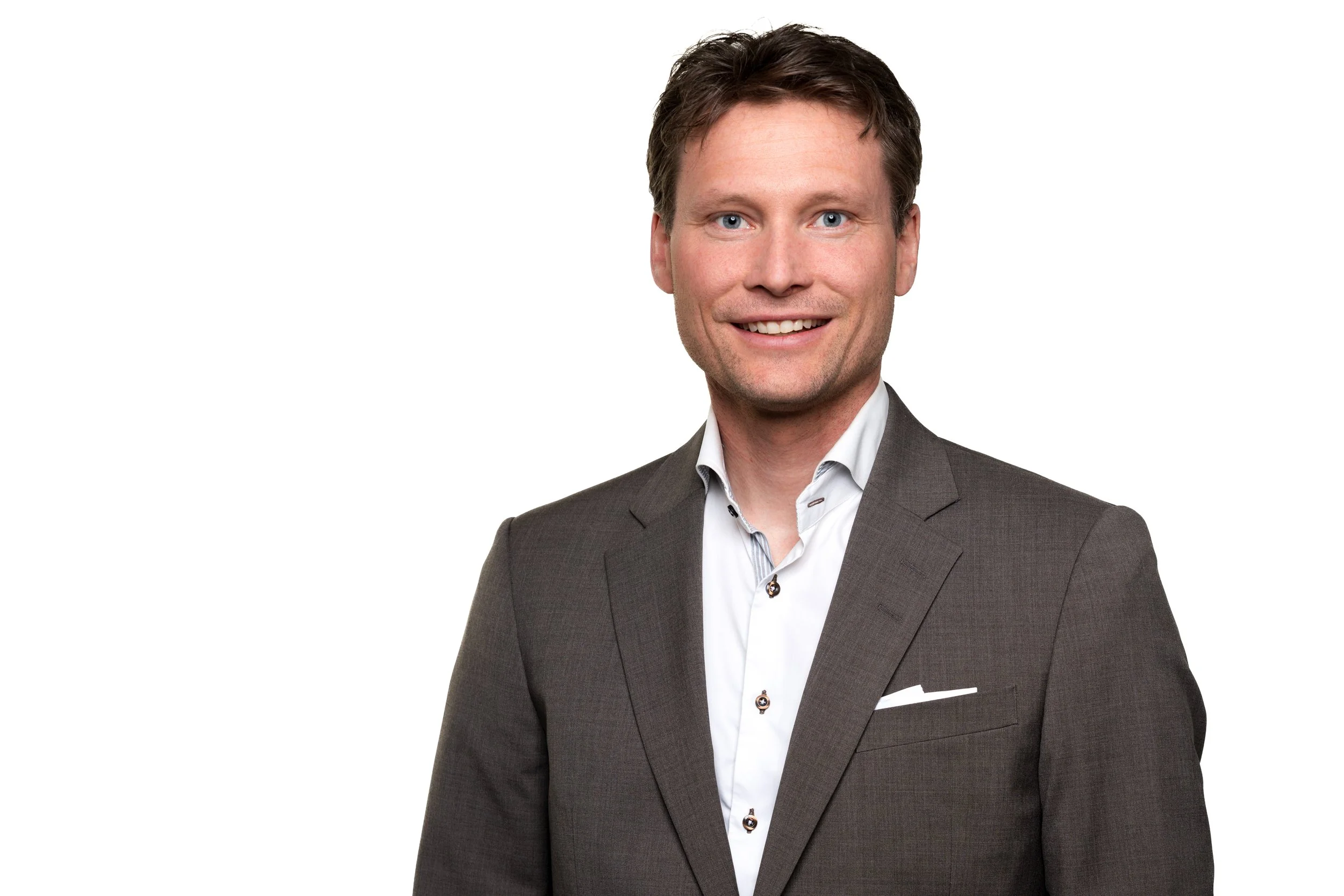 Portrett av en mann i svart dress, hvit skjorte, som smiler, med kort brunt hår.