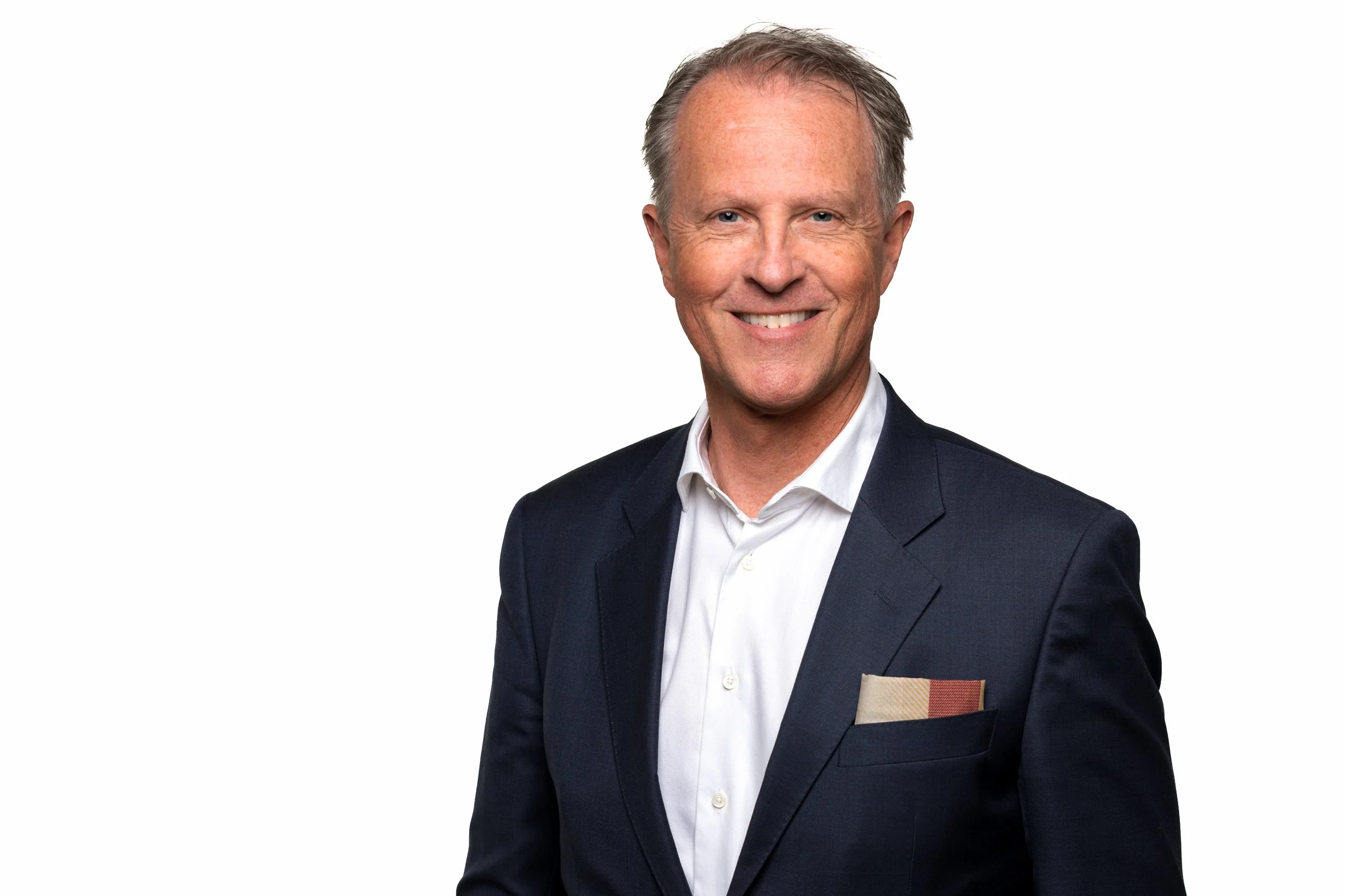 En smilende mann i svart dress og hvit skjorte, med en liten notisbok i frontlommen.