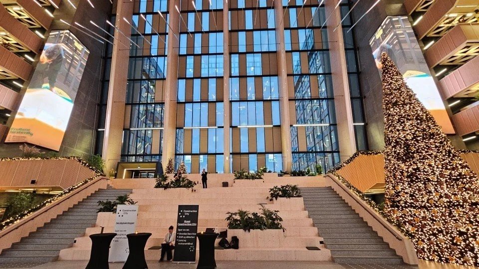 Innendørs atrium med store vinduer, trappetrinn, dekorert juletre med lys, og to store digitale skjermer som viser bilder.