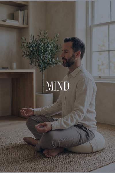 A man practicing meditation in a bright room with a window, a potted plant, and shelves. The word "MIND" is overlayed on the image.