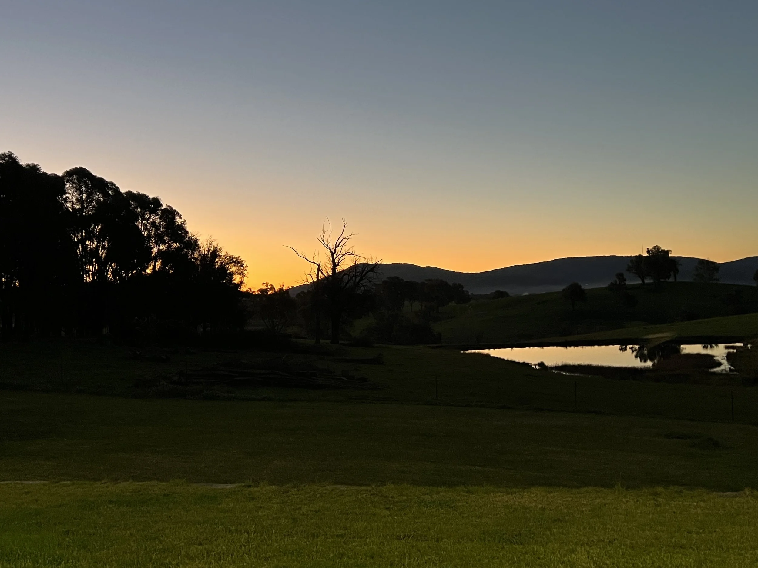 Sunset peaking out from behind the hill in the distance and reflecting off of the dam. 