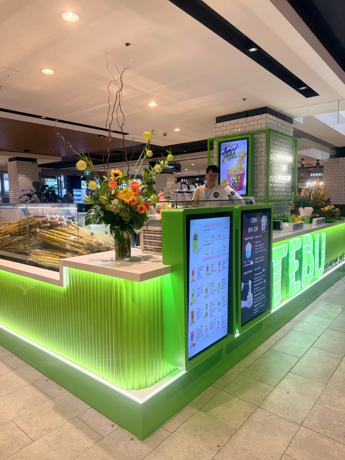 Modern Tebu sugarcane juice kiosk with digital ordering screens and green illuminated counters