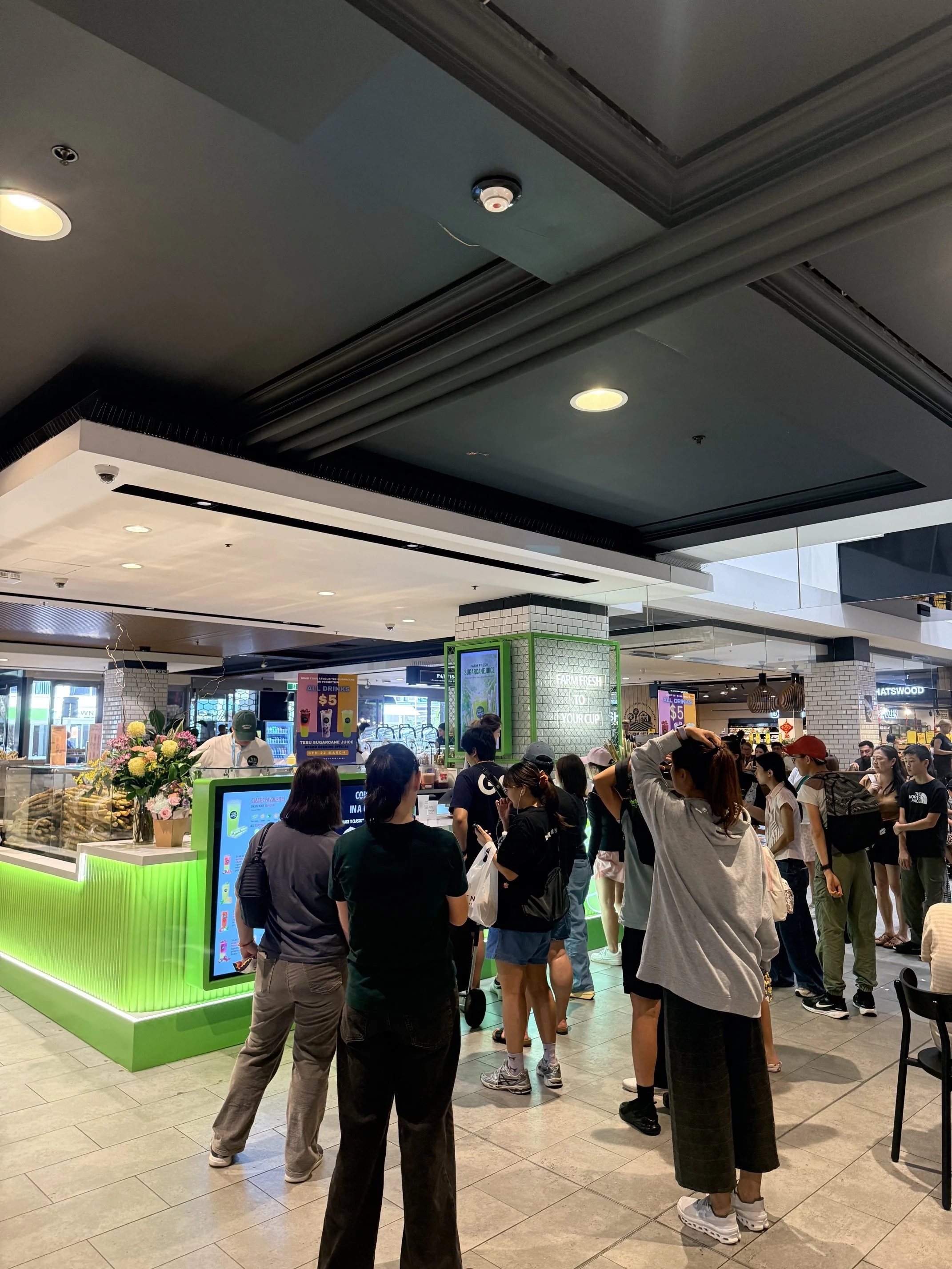Customers gathering at a brightly lit Tebu sugarcane juice kiosk inside a shopping centre