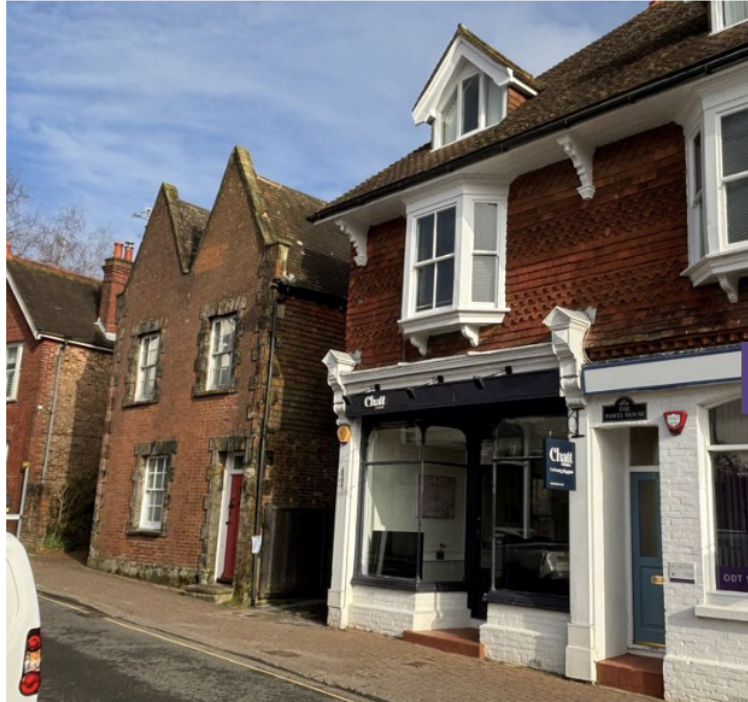 A street view featuring a traditional red brick building with white window frames and a corner shop with a black awning. The shop has a sign that reads 'Clarel.'